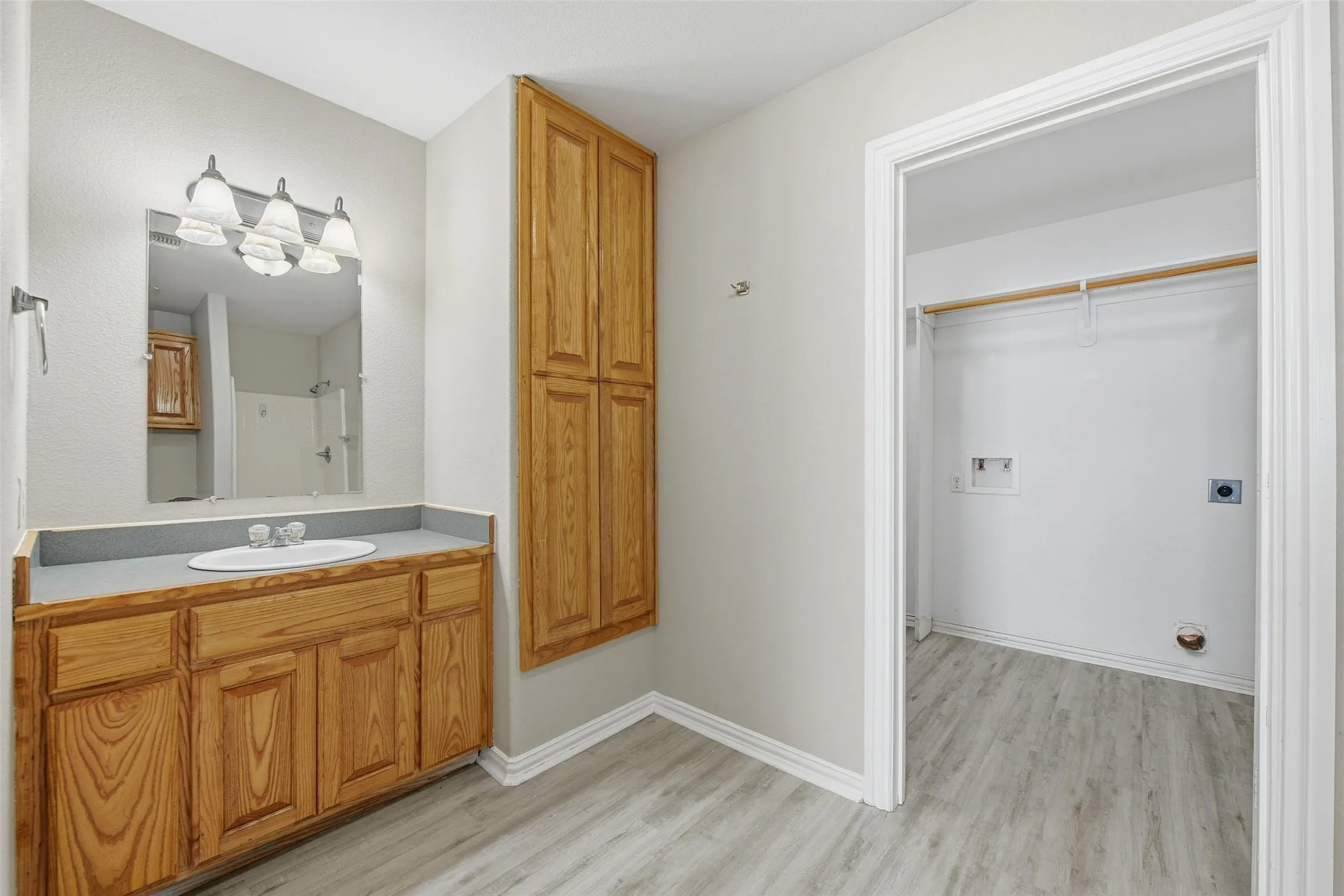 Light wood-finish flooring, vanity with wood cabinetry, wall-mounted wood storage cabinet, and laundry area with clothes rod