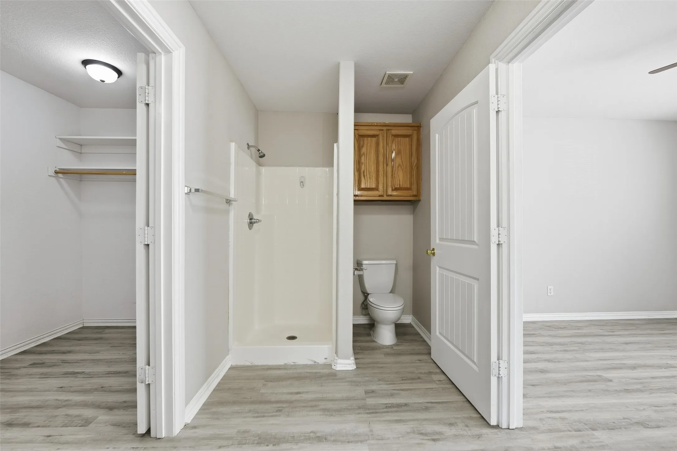 Full bathroom with a standalone shower, toilet, and overhead wood-finish cabinetry
