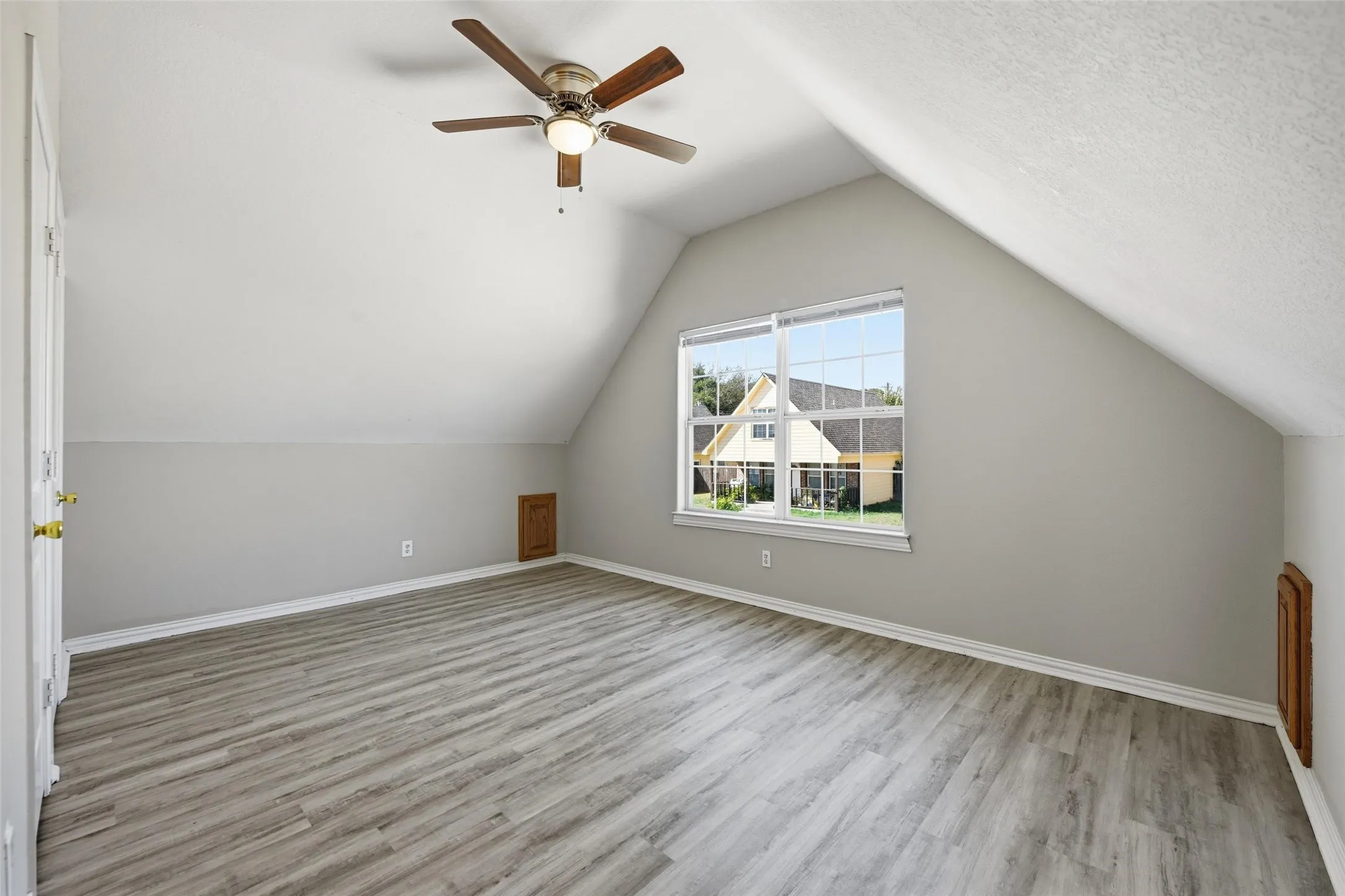 Wood-finish flooring with a vaulted ceiling, a ceiling fan with integrated lighting, and a large window