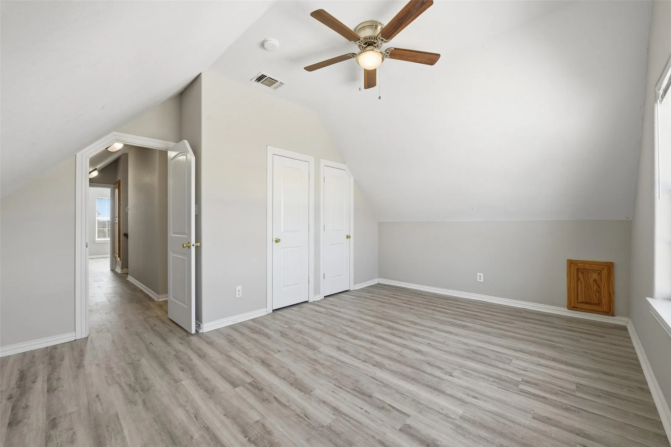 Spacious room featuring wood-finish flooring, two white panel doors, an angled ceiling, and a ceiling fan with light fixture