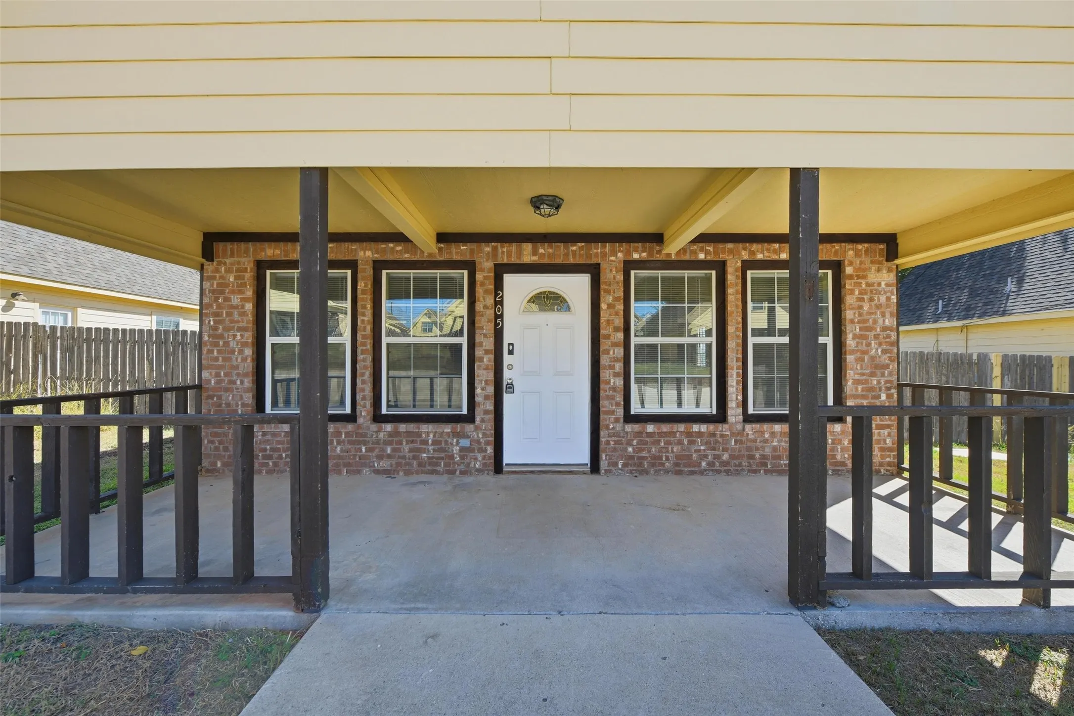 Brick exterior with a covered porch, white entry door with an arched window, and multiple windows featuring dark trim