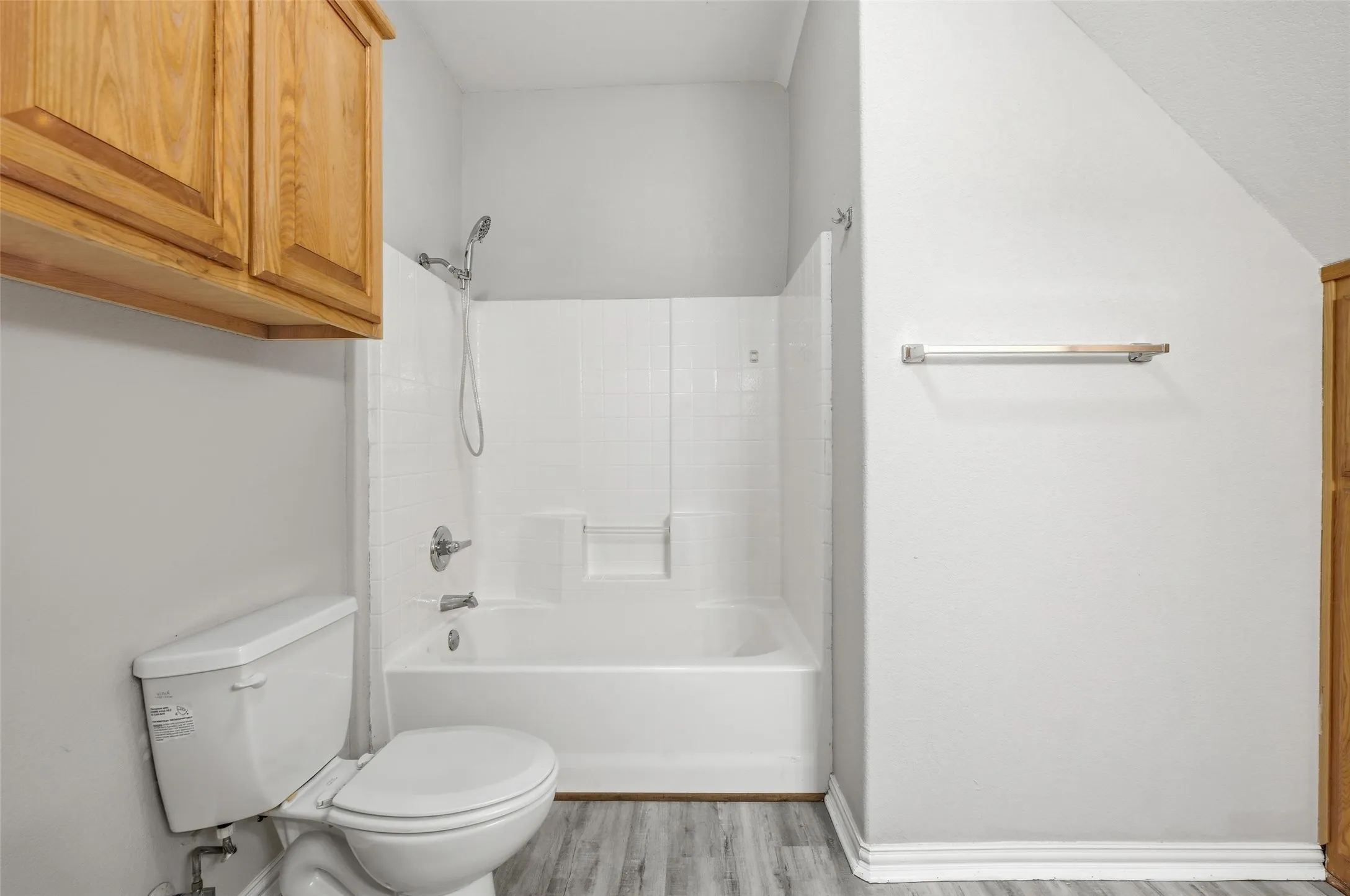 White bathtub with shower, toilet, and wood-finish flooring