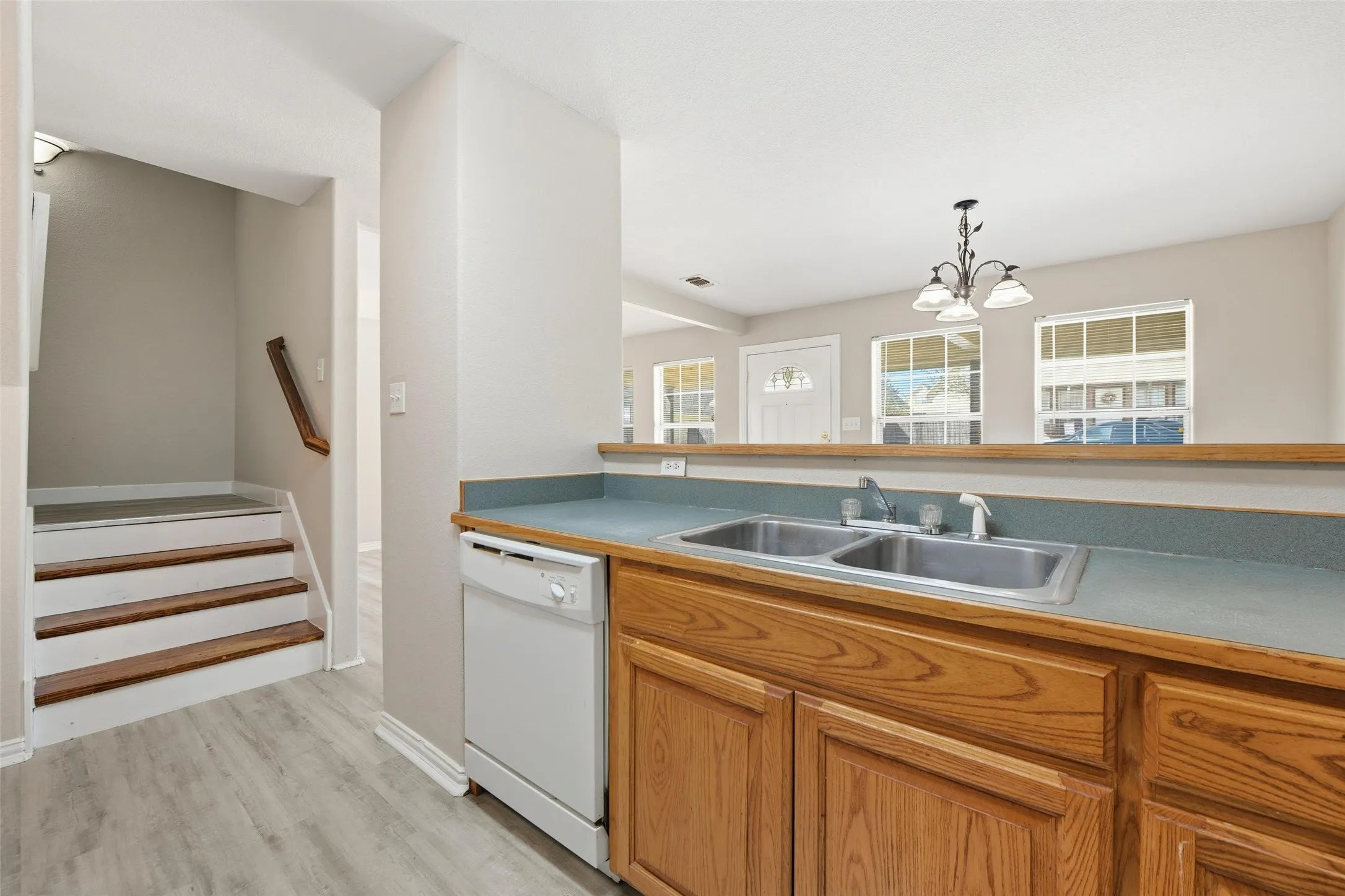 Wood-finish flooring, two-compartment stainless steel sink, wood cabinetry, white dishwasher, and staircase with wood handrail