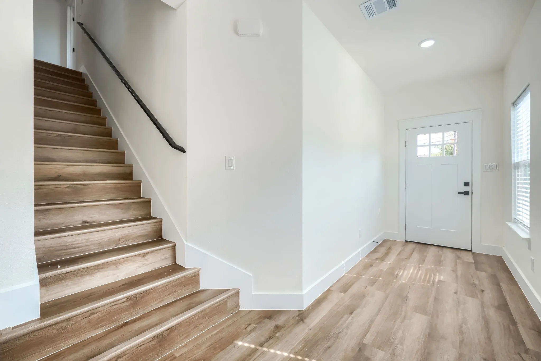 Wood-finish flooring throughout, white interior walls, recessed lighting, and a white entry door with glass paneling
