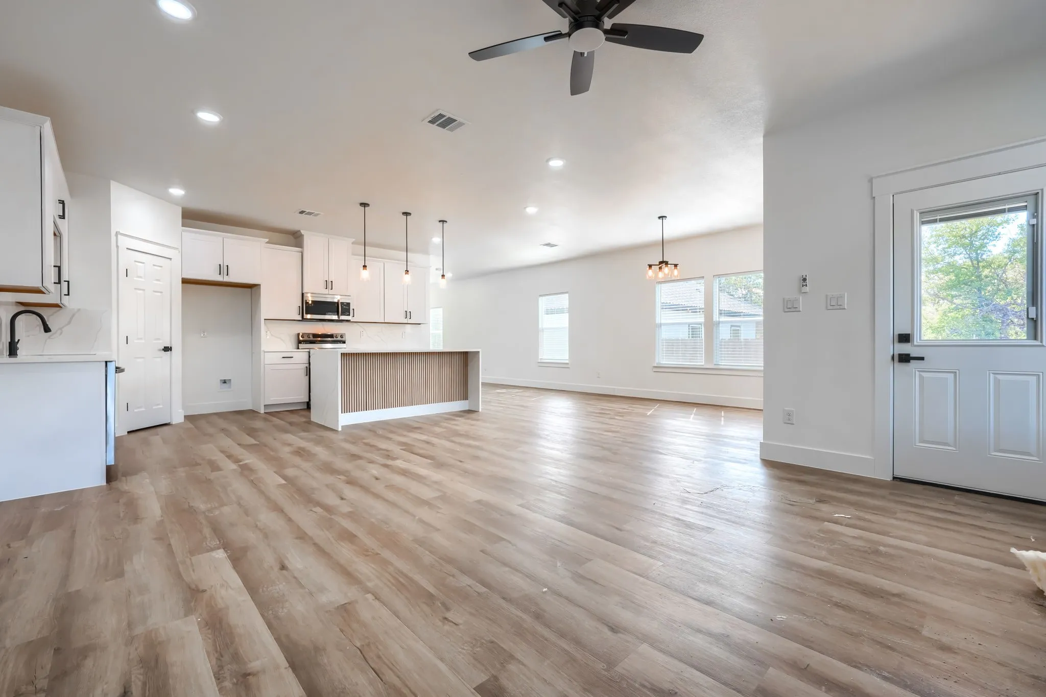 Wood-finish flooring throughout, white cabinetry with black hardware, kitchen island with wood-finish paneling, pendant lighting, and recessed ceiling lights