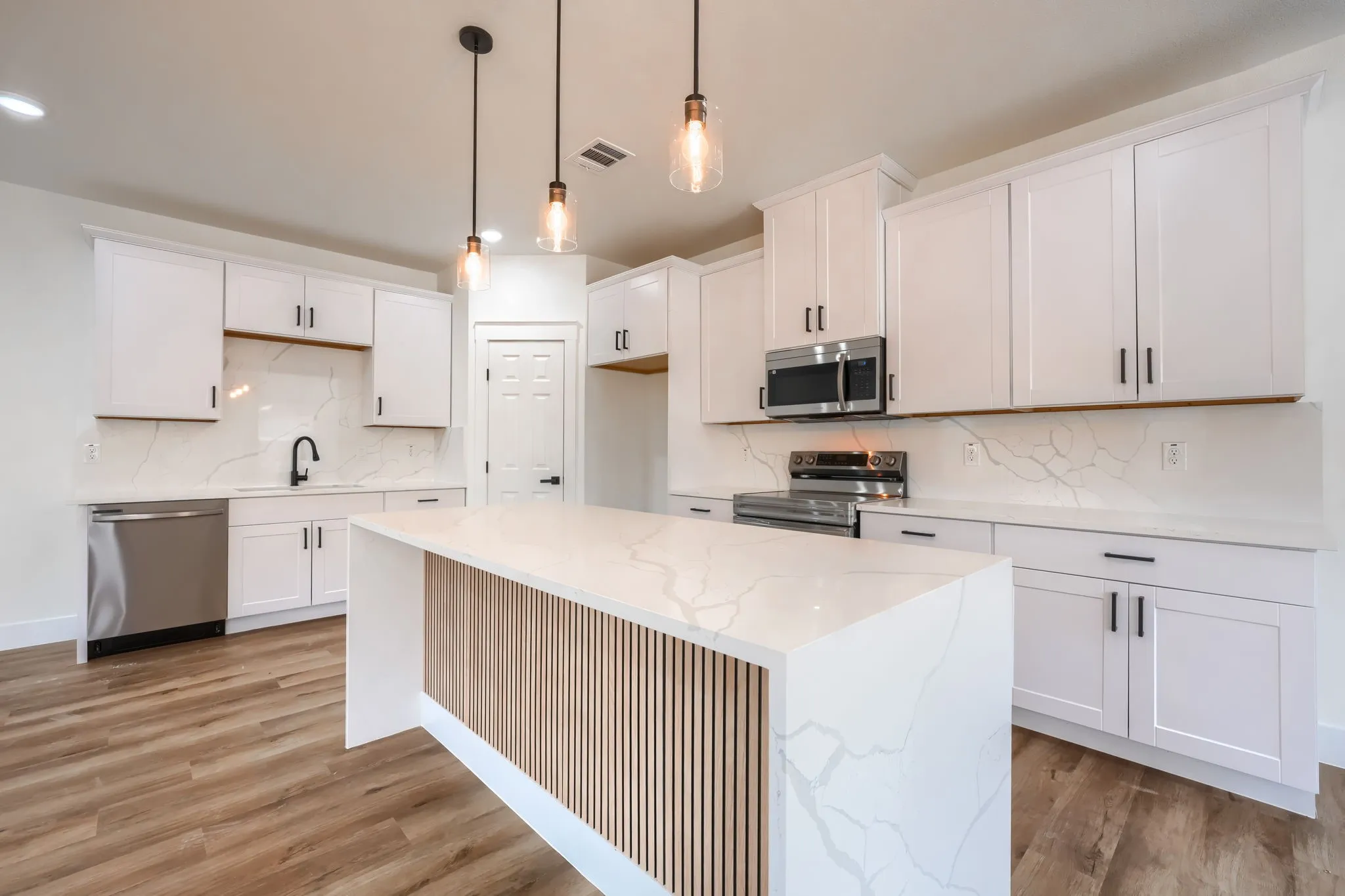 Kitchen featuring white cabinetry, stainless steel appliances, a large island with a slatted wood-finish accent panel, and pendant lighting