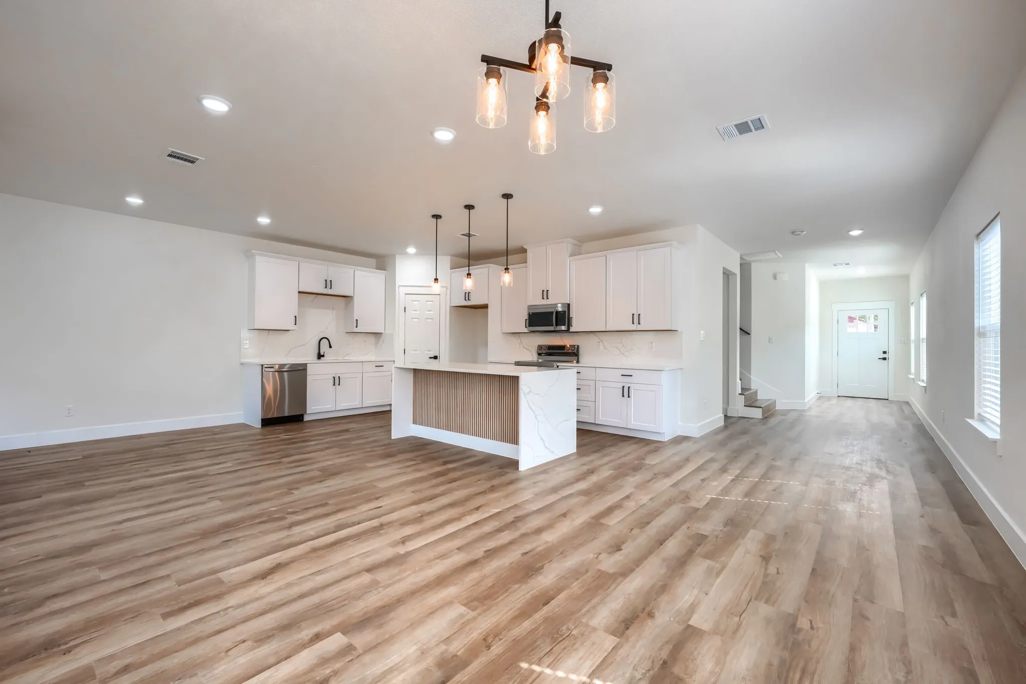 Wood-finish flooring throughout, kitchen with white cabinetry and light countertops, stainless steel appliances, and a central island with pendant lighting