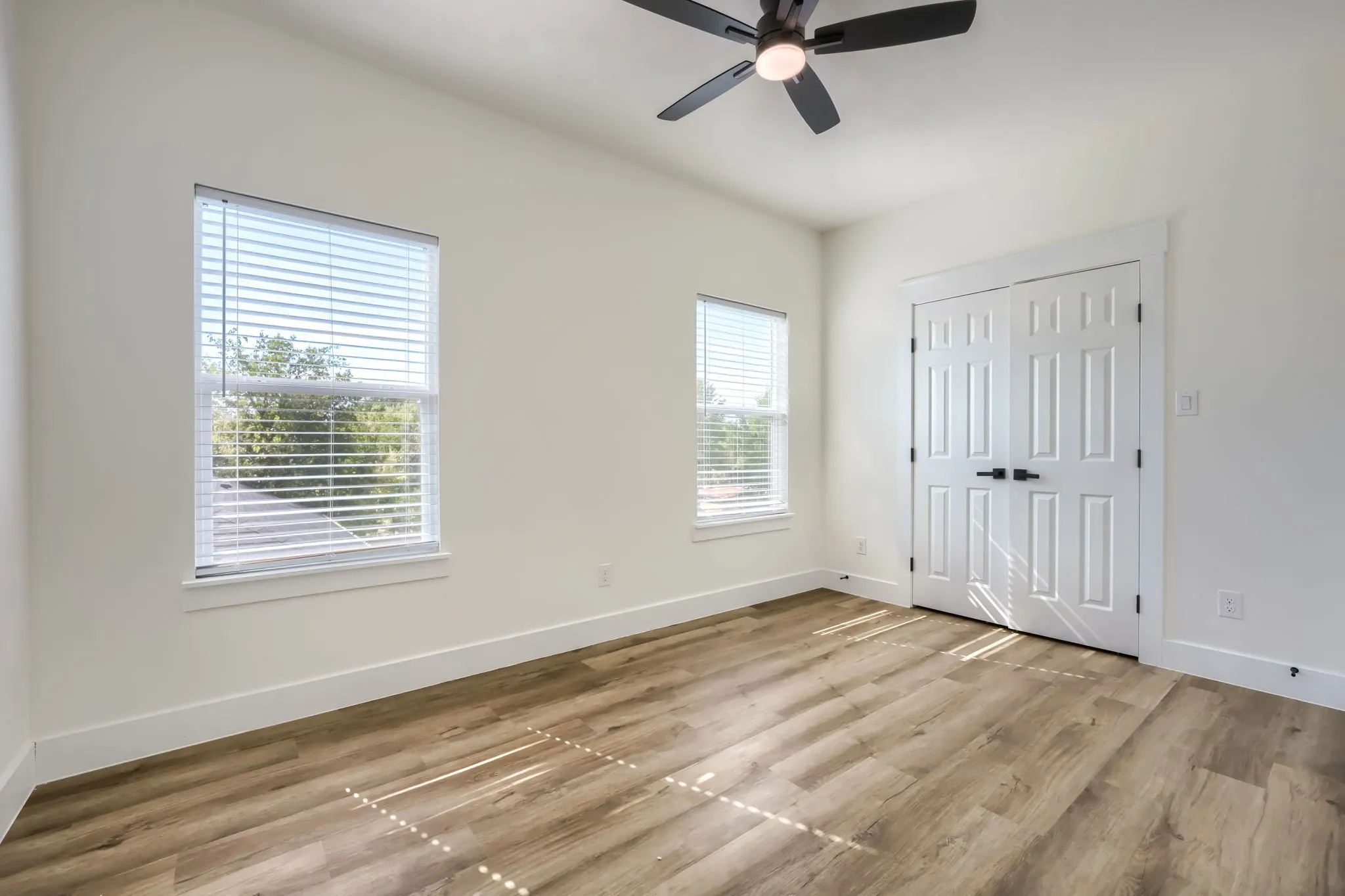 Wood-finish flooring, white walls, two windows with blinds, bi-fold doors, and a ceiling fan