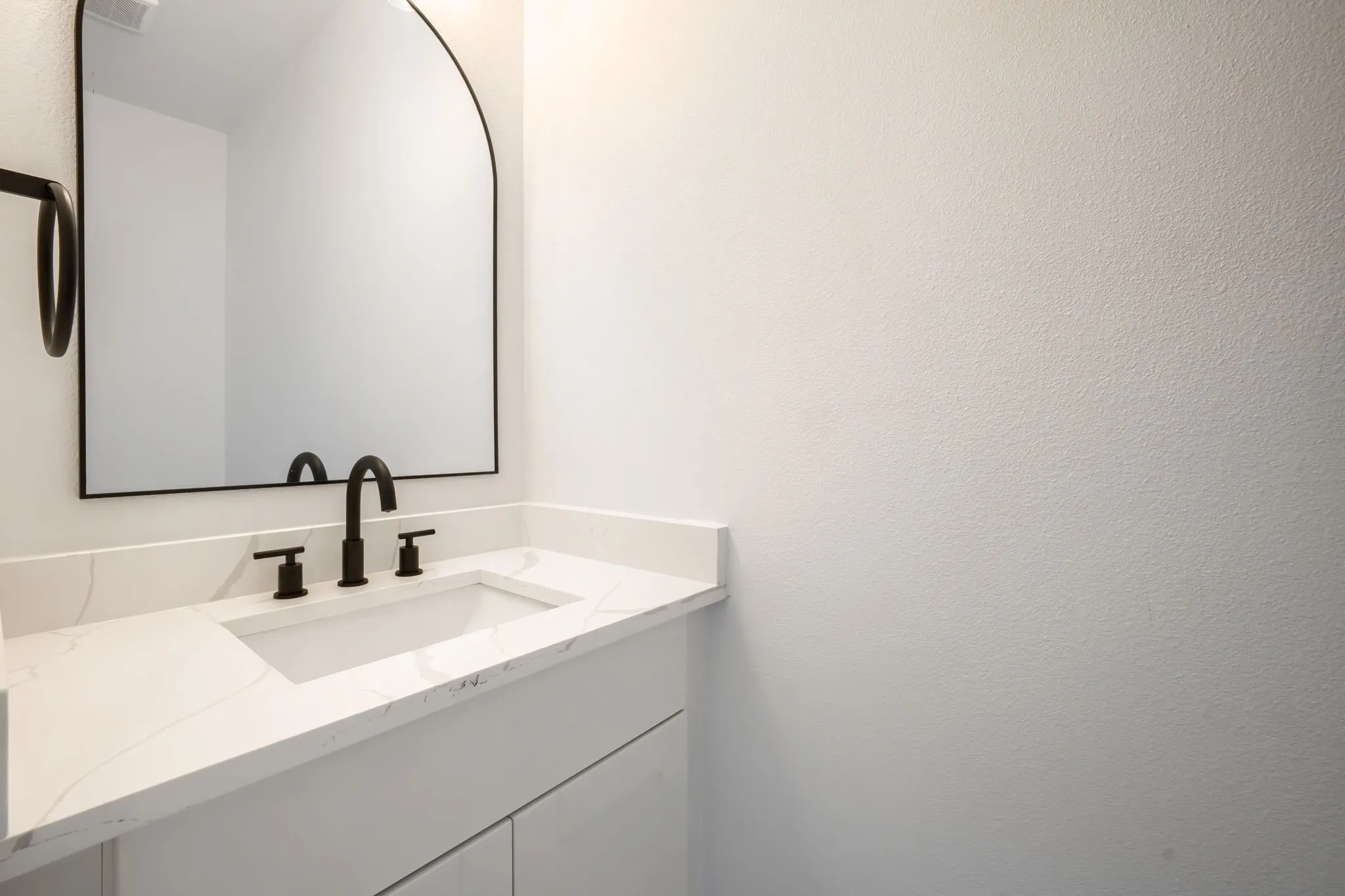 White vanity with a rectangular undermount sink, matte black faucet, and white countertop