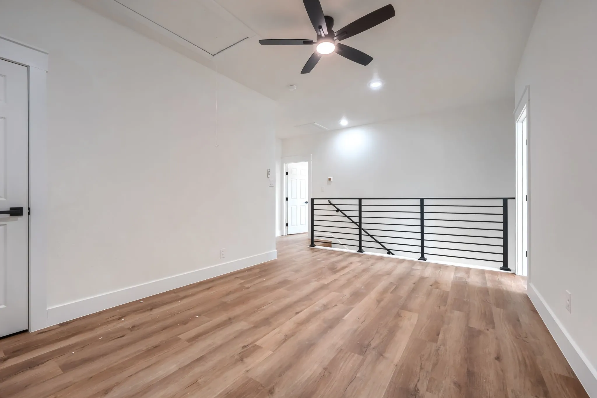 Wood-finish flooring, contemporary black metal railing, white walls, recessed lighting, and a ceiling fan with light fixture