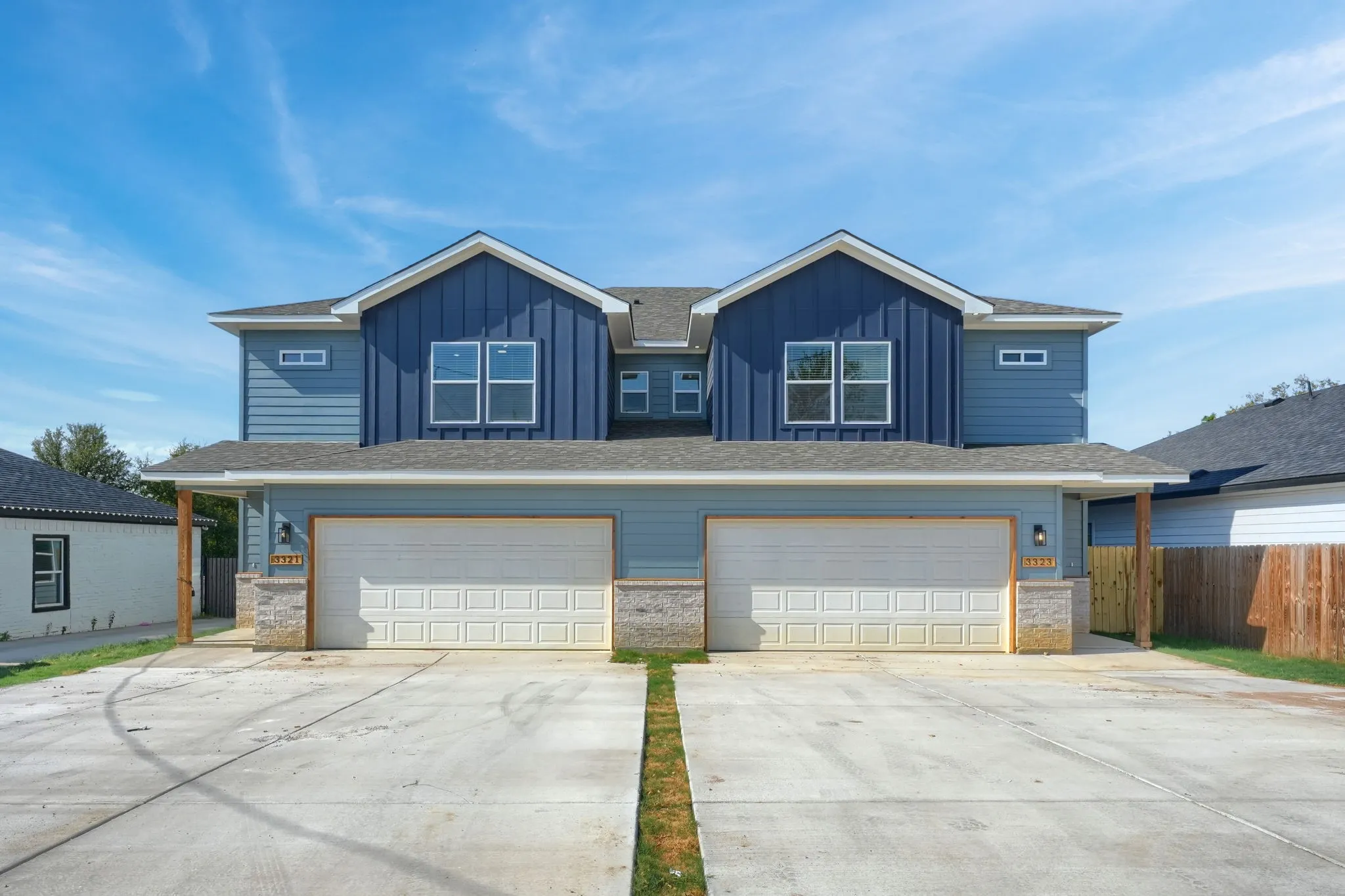 Two-story duplex with light blue siding, dark blue vertical siding accents, and a stone veneer foundation