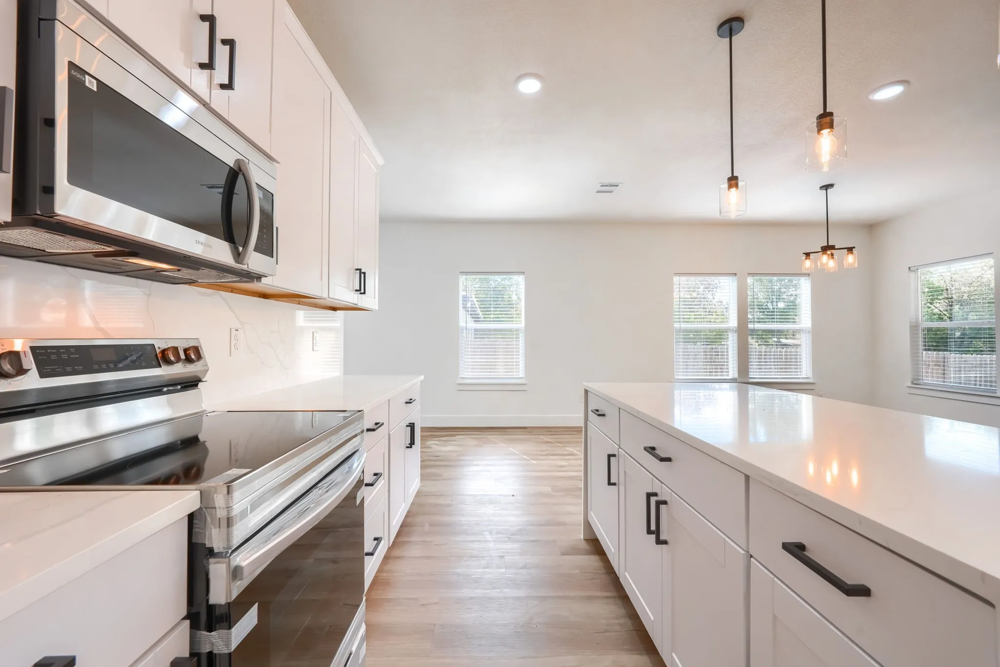 Kitchen featuring stainless steel appliances, white cabinetry with matte black hardware, white countertops, and wood-finish flooring