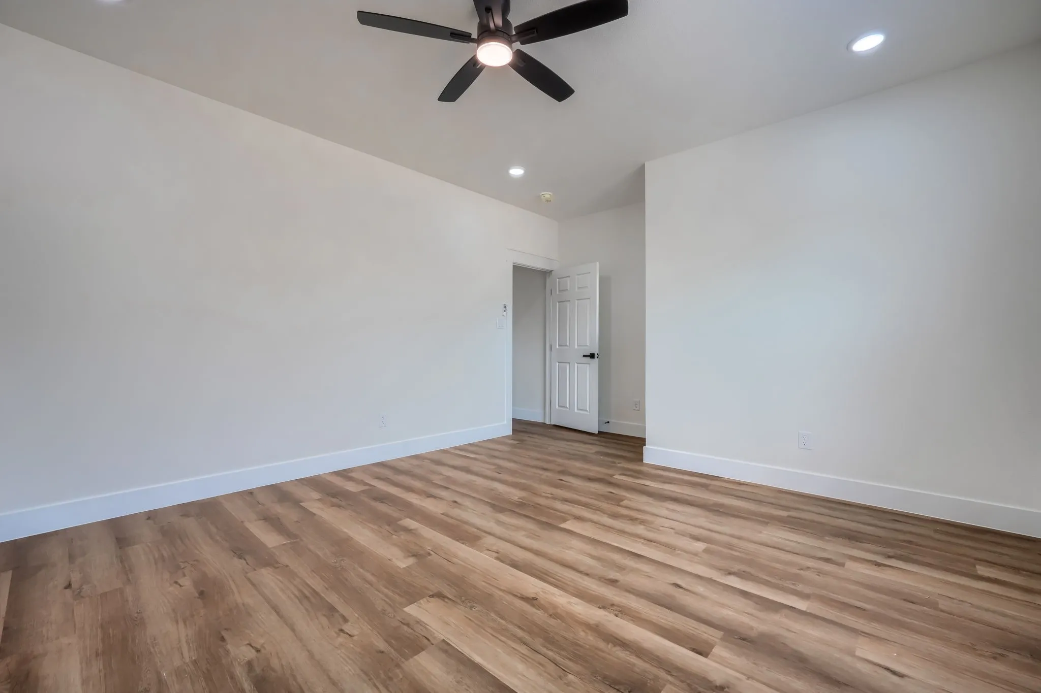Wood-finish flooring, recessed lighting, ceiling fan, white paneled door, and neutral wall tones