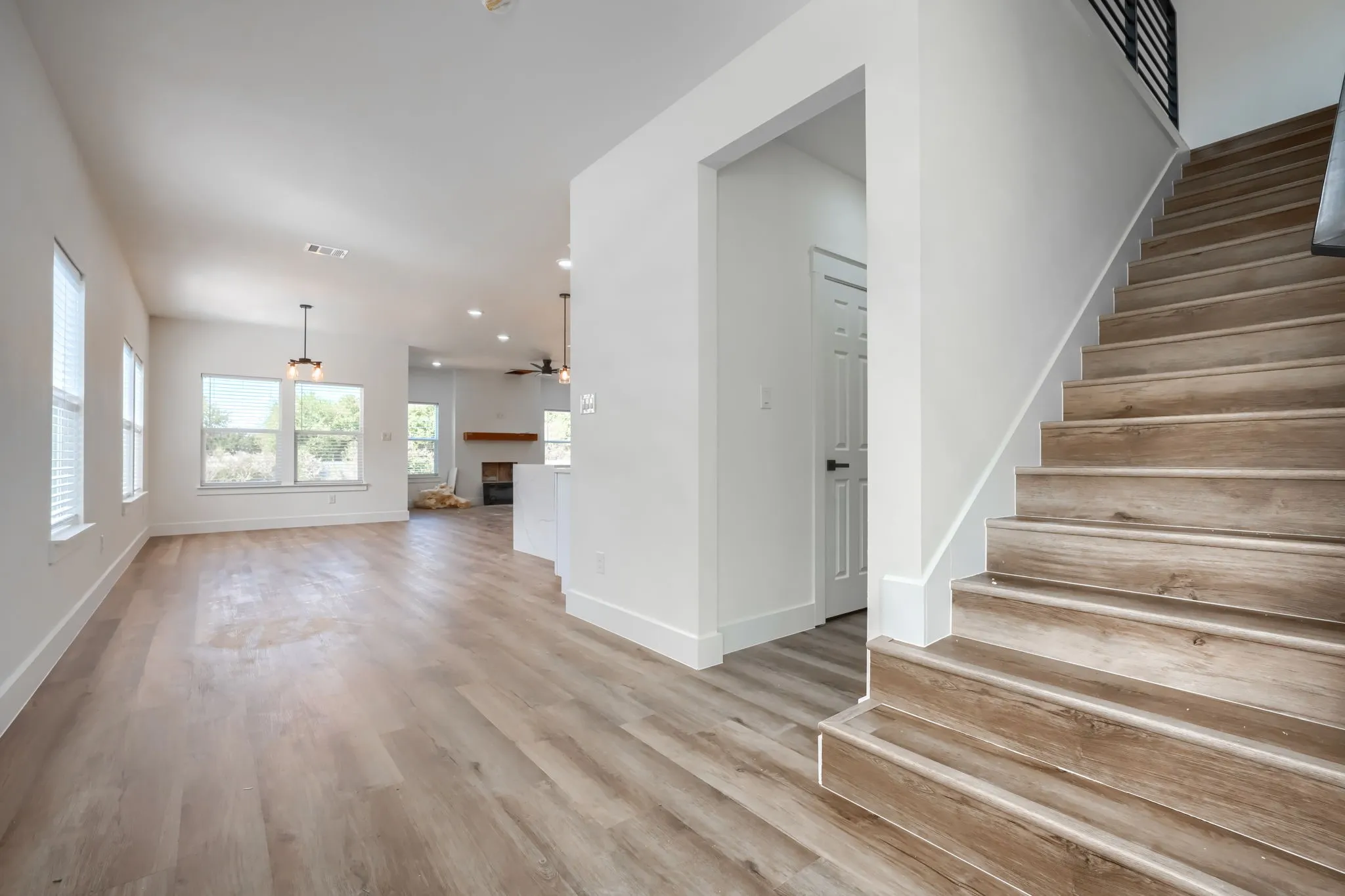 Wood-finish flooring throughout, bright white walls, and a staircase featuring wood-finish treads with a modern black railing