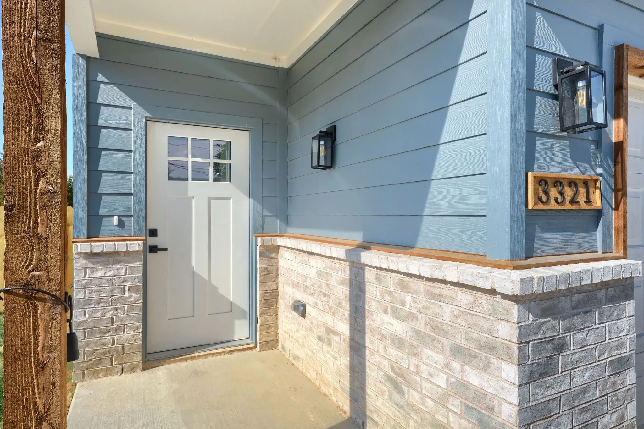 Light blue siding exterior featuring a white paneled door with glass inserts, brick-finish wainscoting, and black exterior lighting fixtures