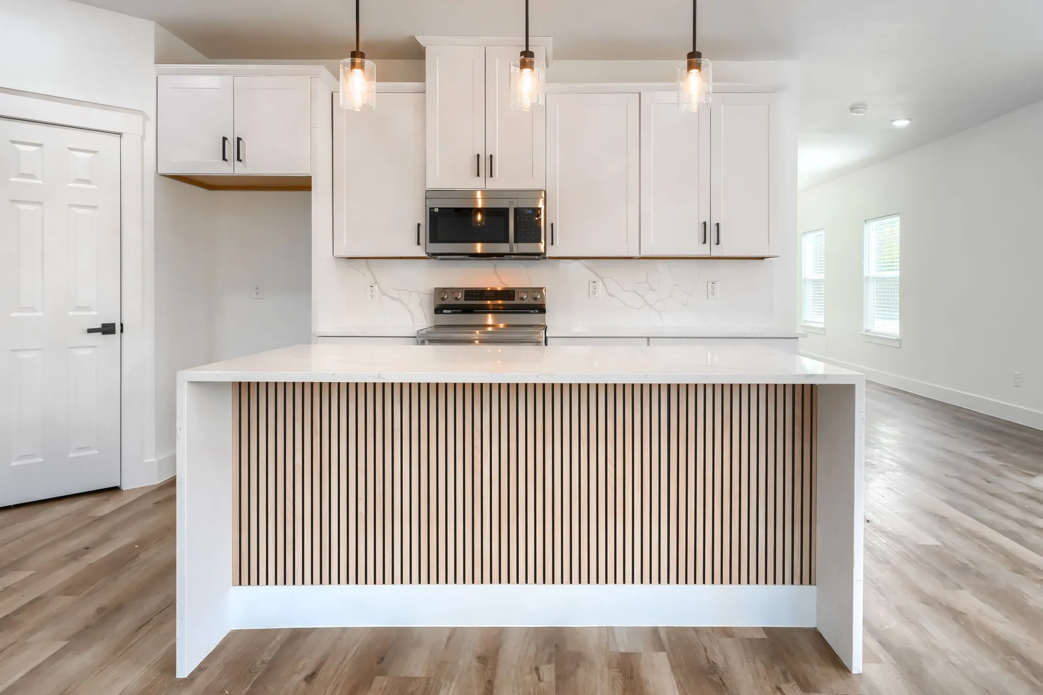Kitchen featuring white cabinetry, stainless steel microwave, integrated electric stove, white countertops, and a kitchen island with vertical wood paneling