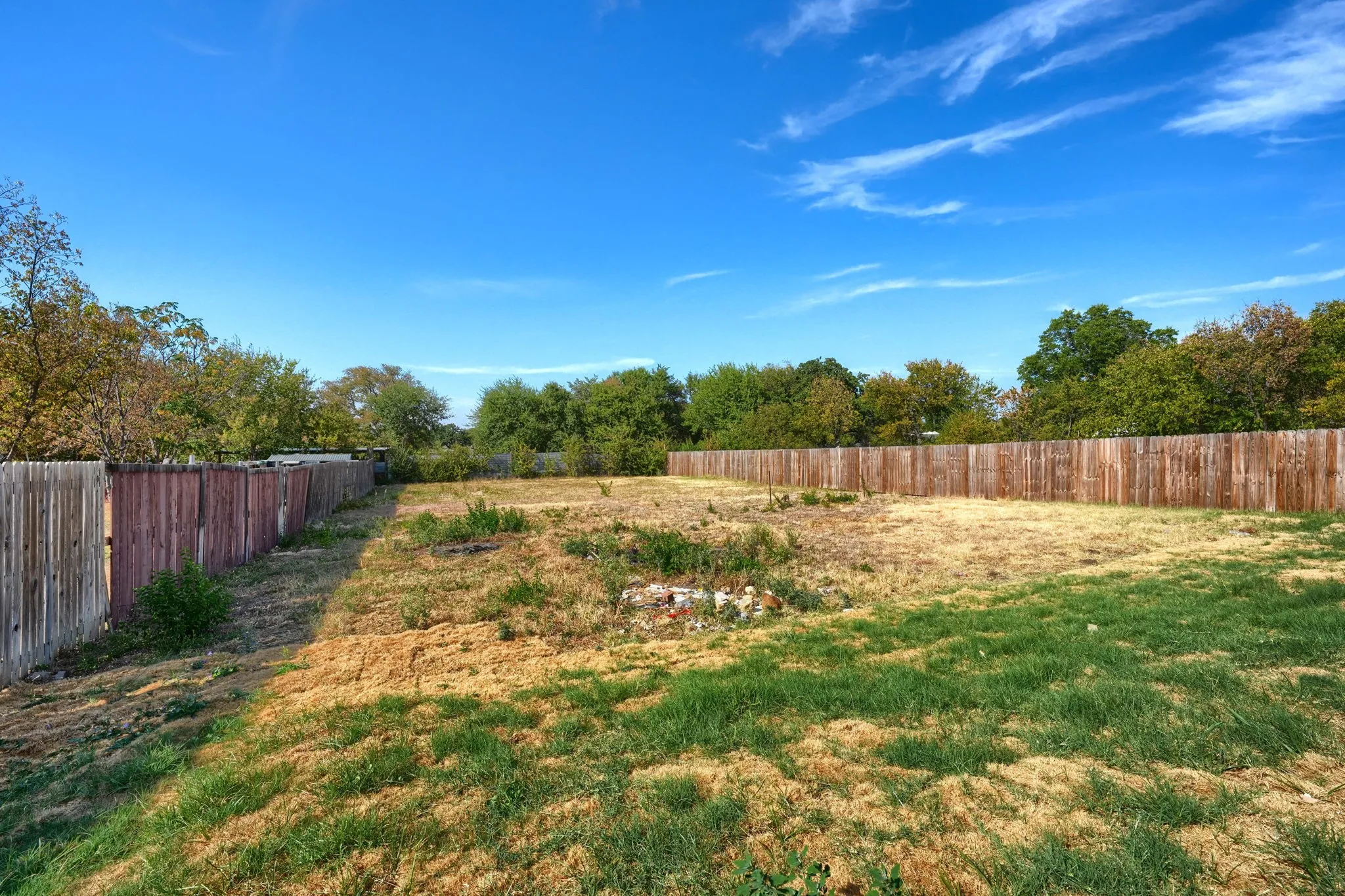 Expansive cleared lot with perimeter fencing and mature trees