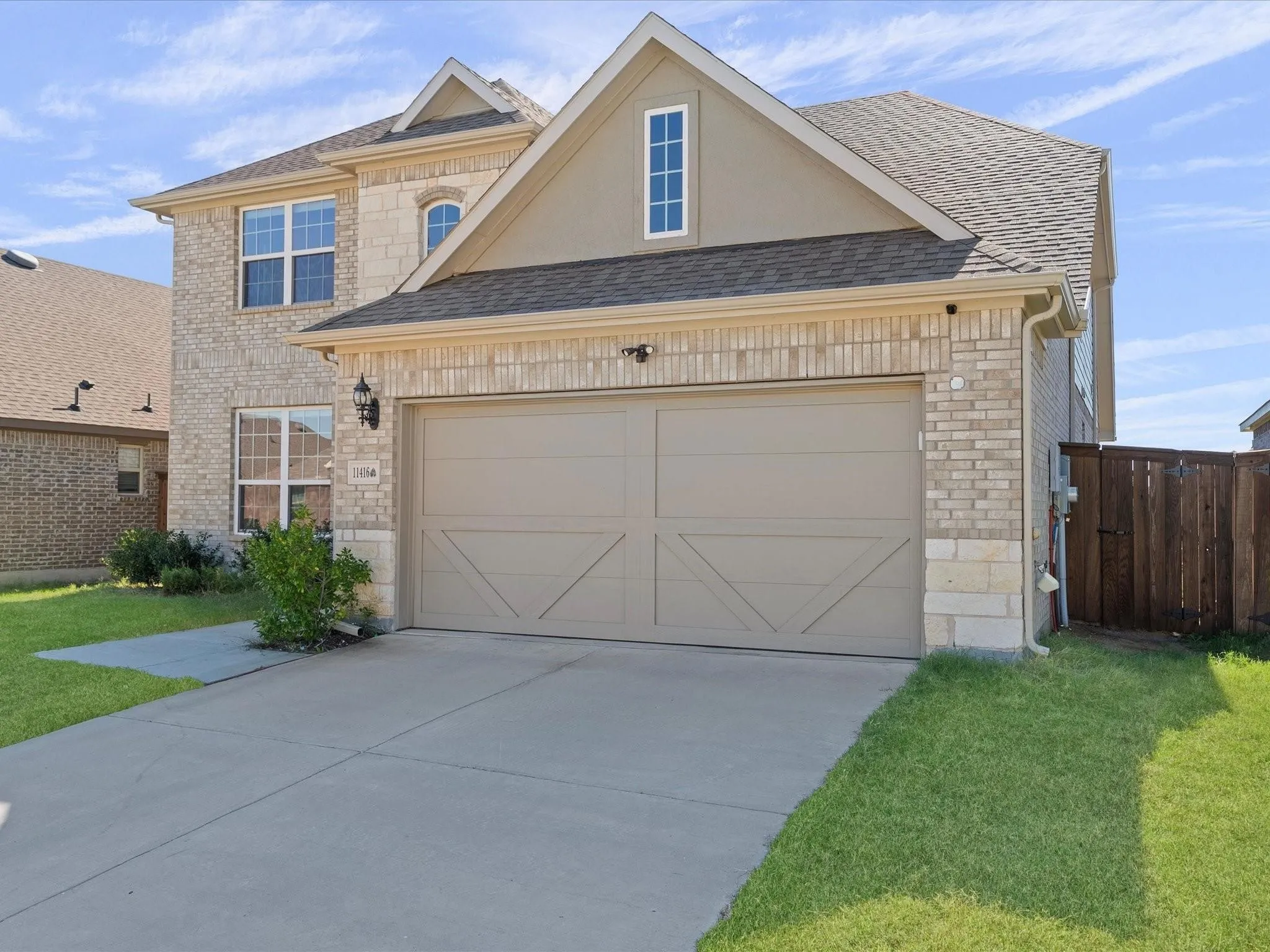 Brick and stone exterior with a two-car garage, concrete driveway, and established landscaping