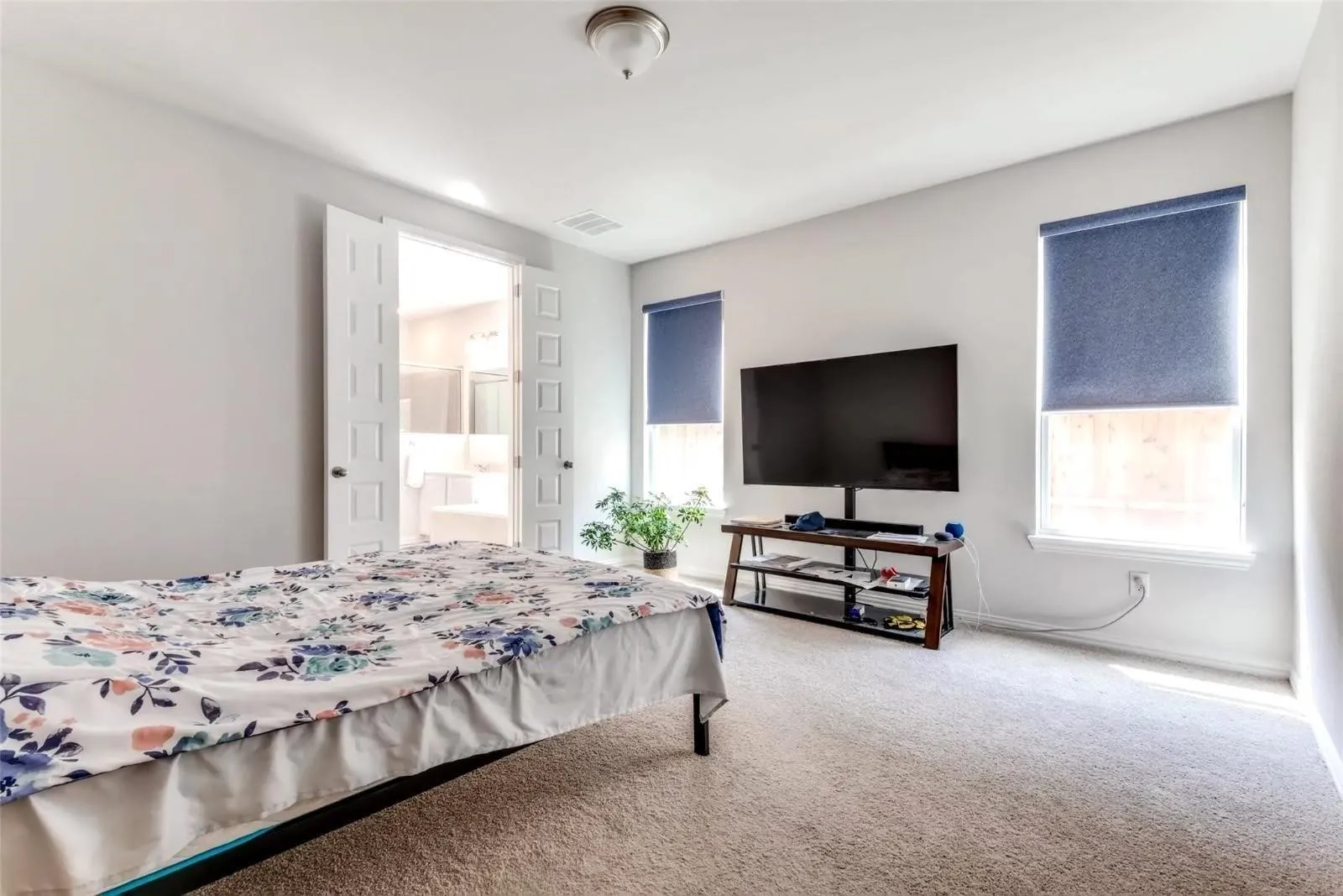 Carpeted room featuring dual windows with roller shades, a ceiling-mounted light fixture, and double doors opening to an adjoining space