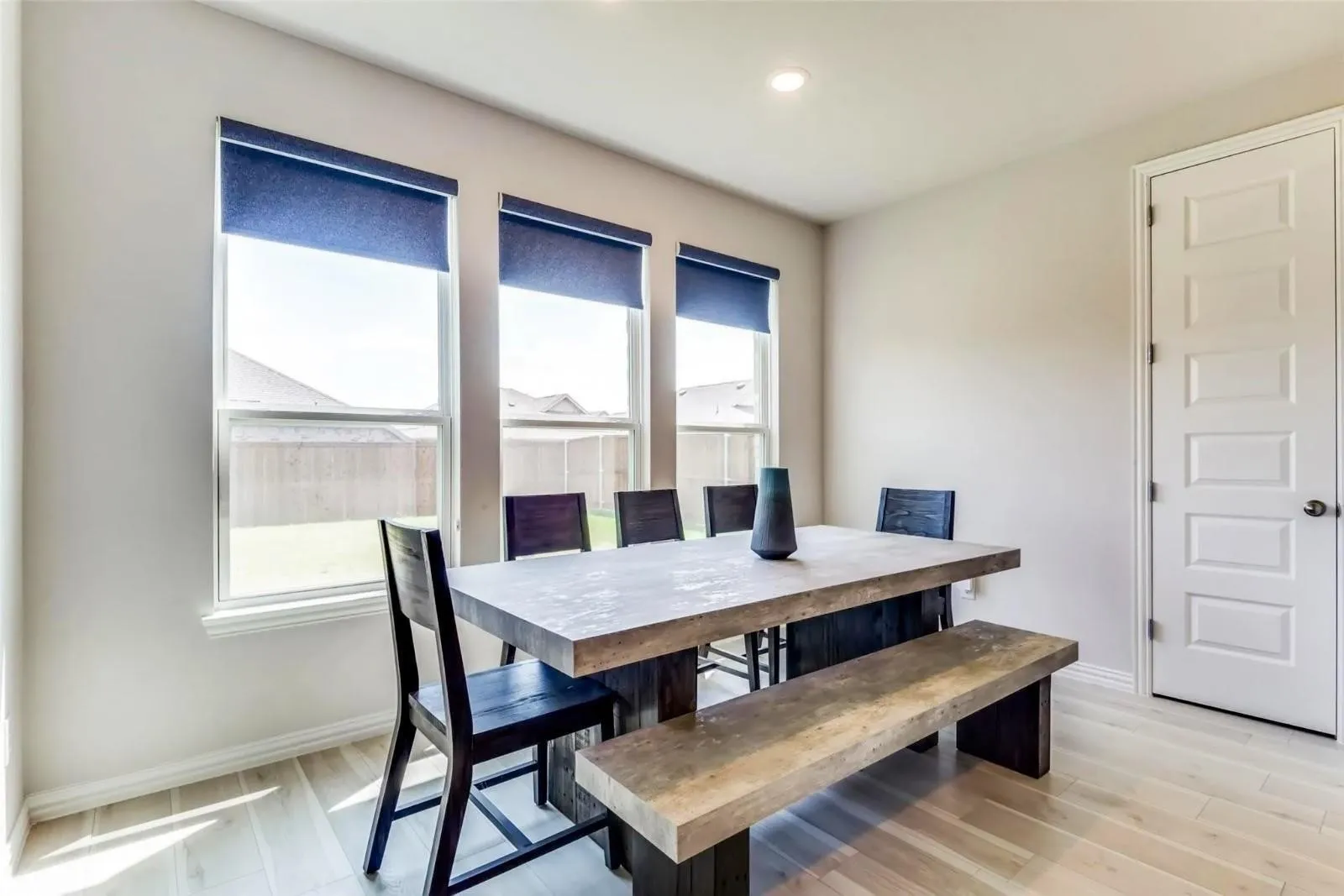 Recessed ceiling lighting, three double-pane windows with roller shades, light wood-finish flooring, and a five-panel interior door