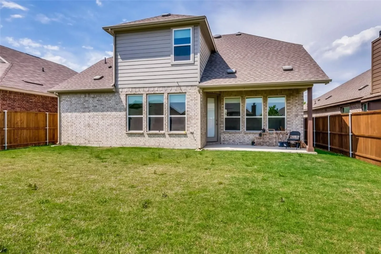 Expansive grassy yard with a covered concrete patio, brick exterior, and wood fencing