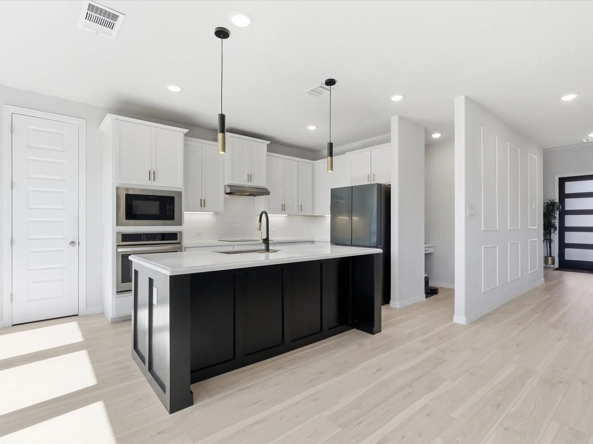 Contemporary kitchen with a central island, stainless steel appliances, light wood-finish flooring, recessed lighting, and a paneled accent wall