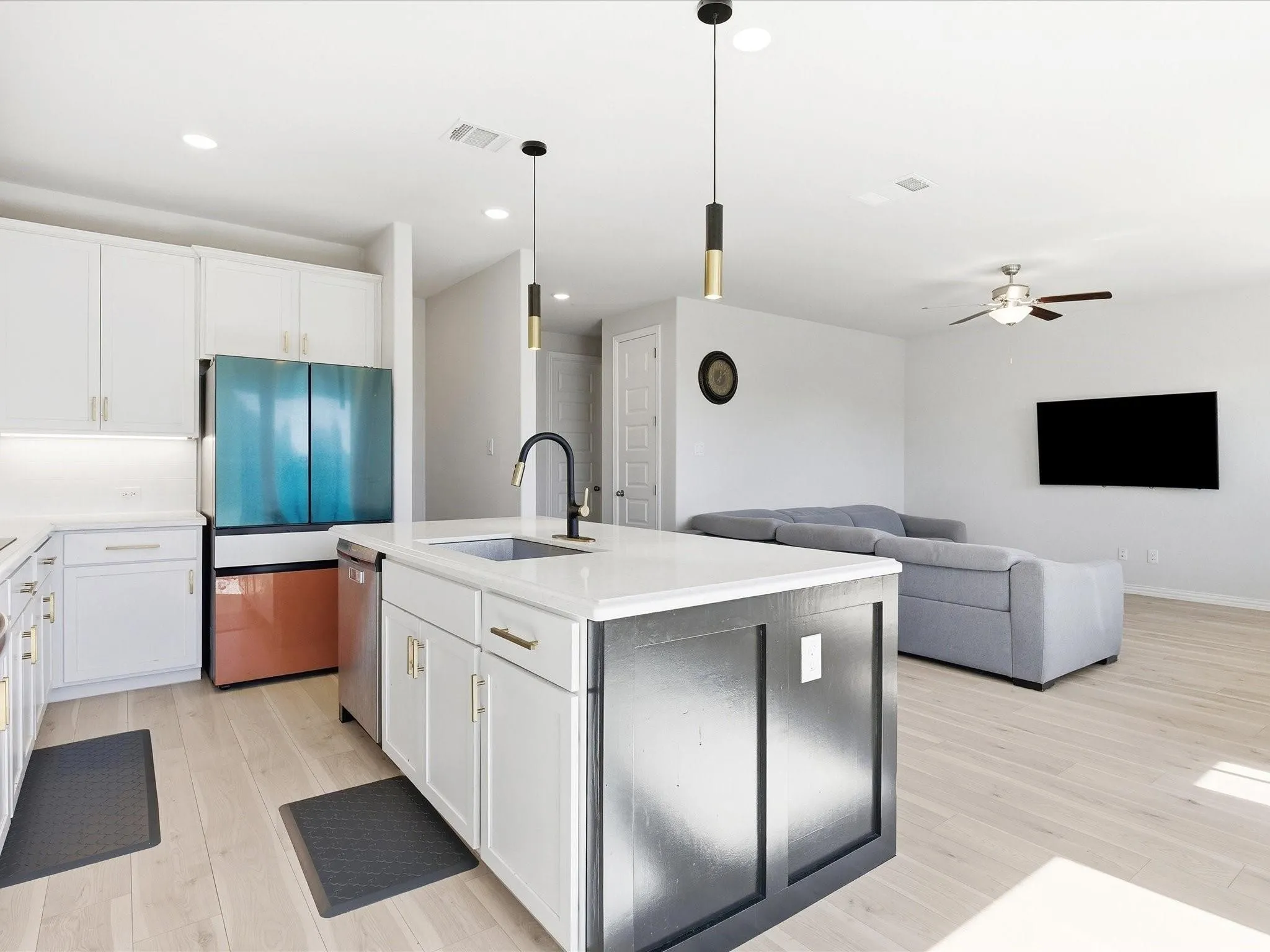 Open-concept living area featuring light wood-finish flooring, white upper and lower cabinetry, a center island with sink, and recessed lighting