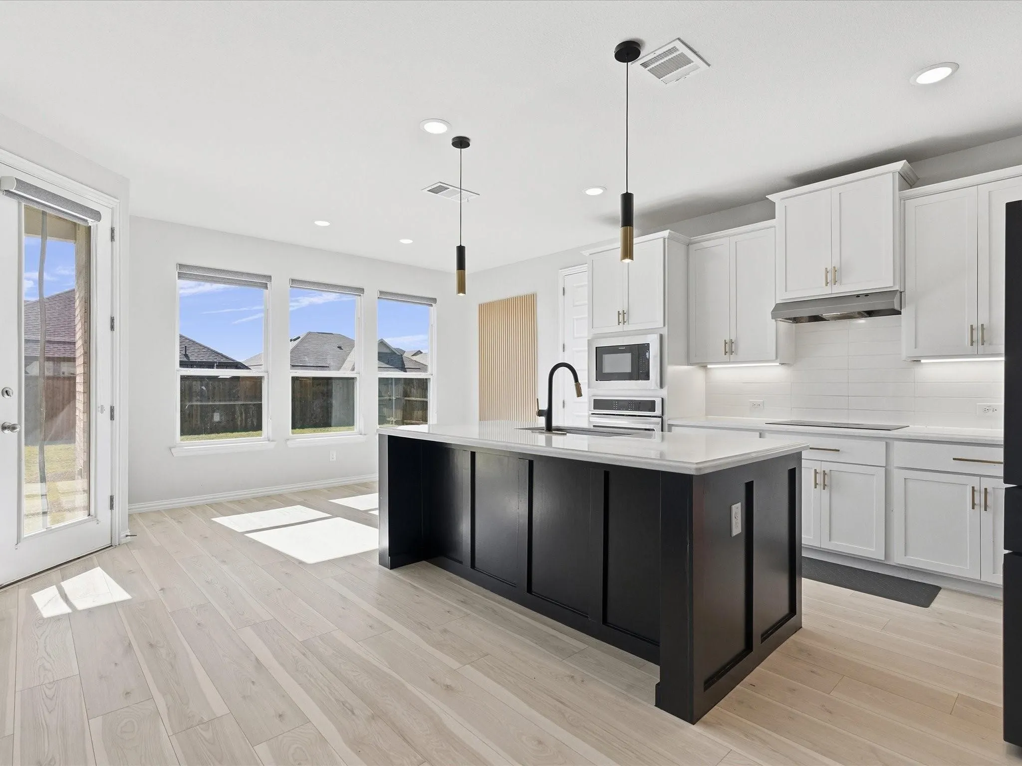Bright kitchen featuring a dark island with a light countertop, light wood-finish flooring, white cabinetry, and recessed lighting