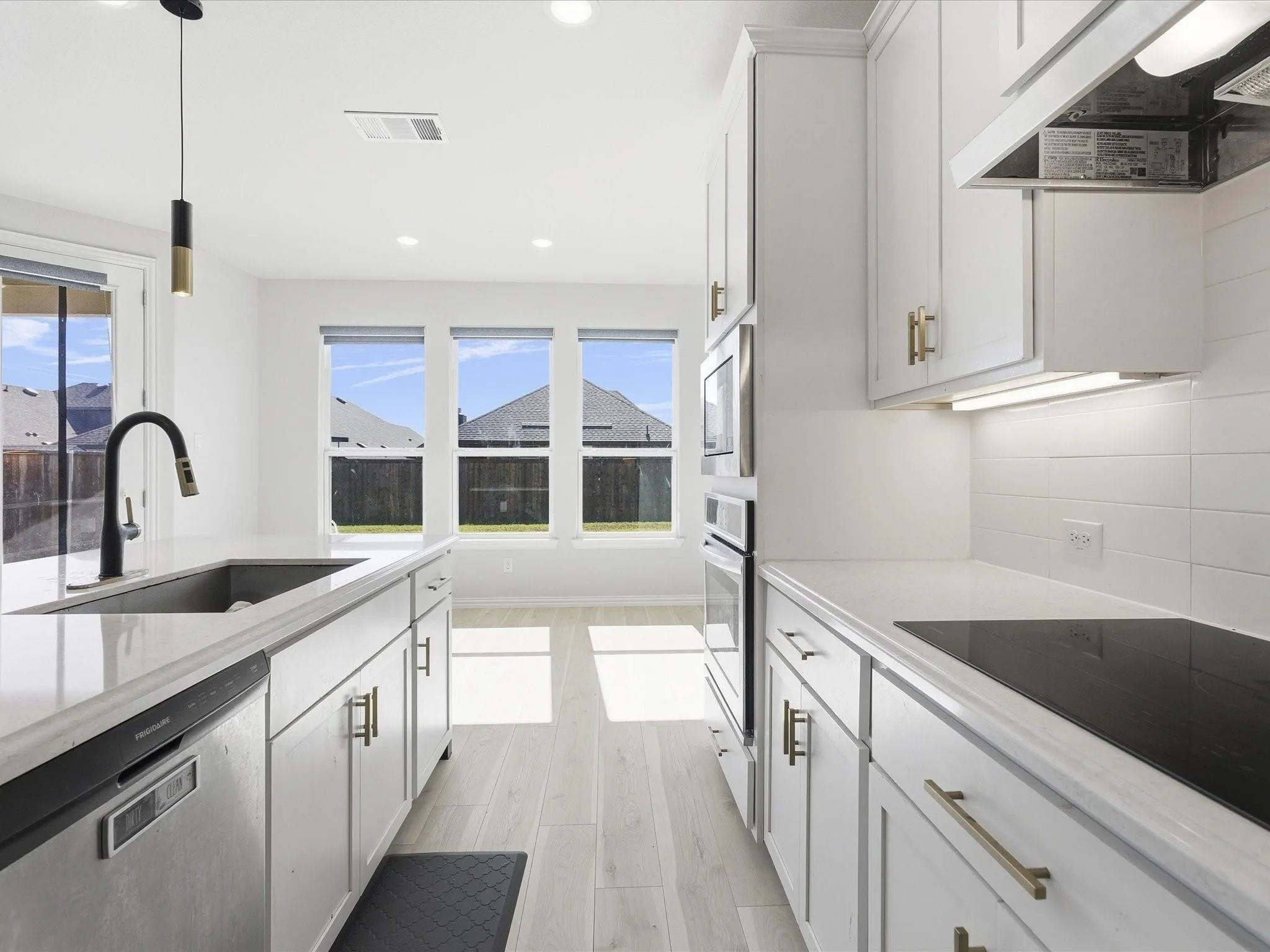 White cabinetry with gold-tone hardware, wood-finish flooring, built-in stainless steel appliances, and a black gooseneck faucet