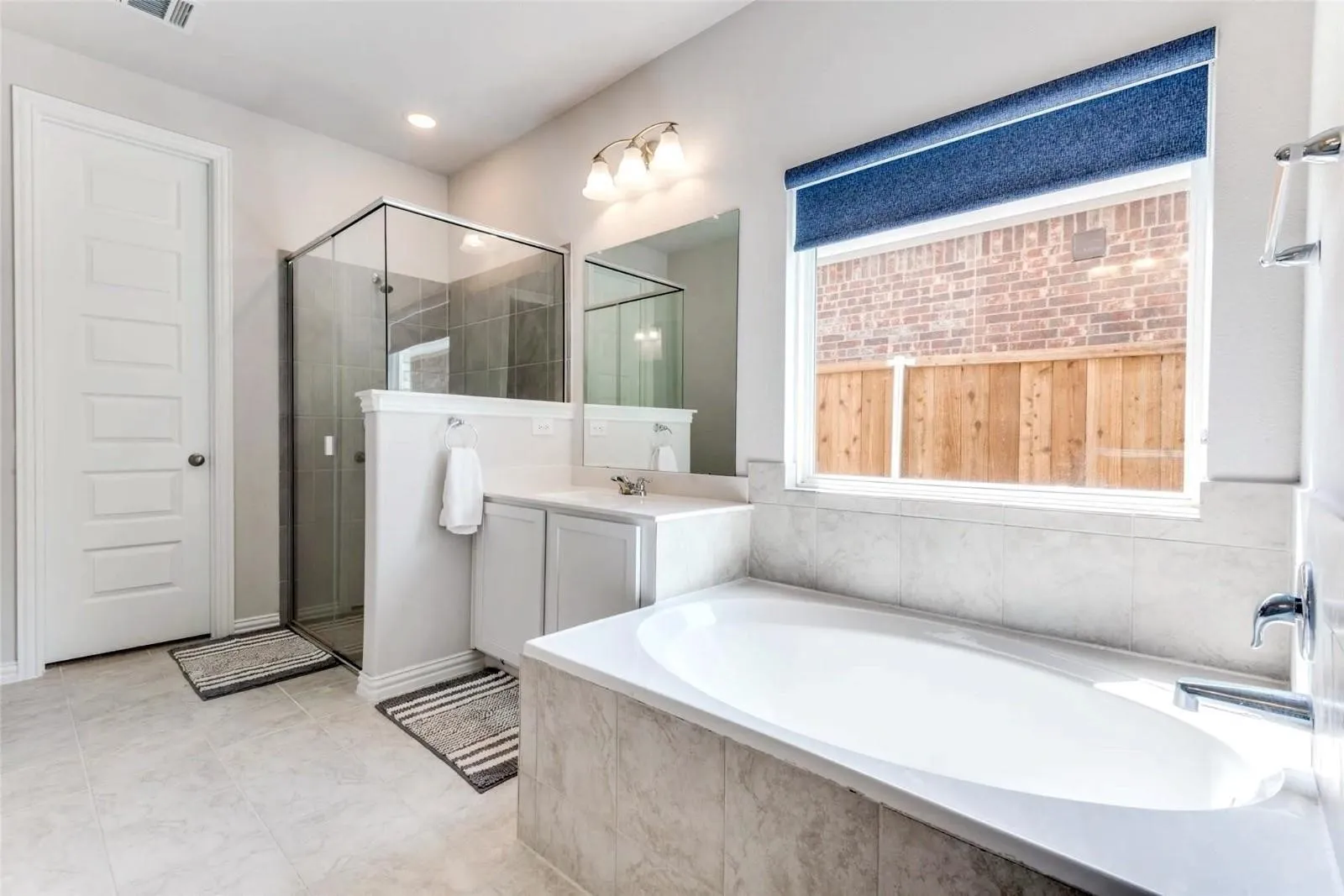 Freestanding soaking tub with tile surround, glass-enclosed shower, dual vanity with undermount sink, and recessed lighting