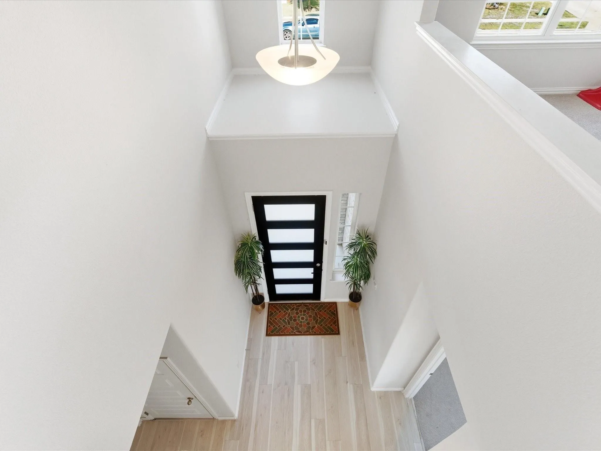 Two-story foyer with light wood-finish flooring, a modern pendant light fixture, and a dark entry door with horizontal lites