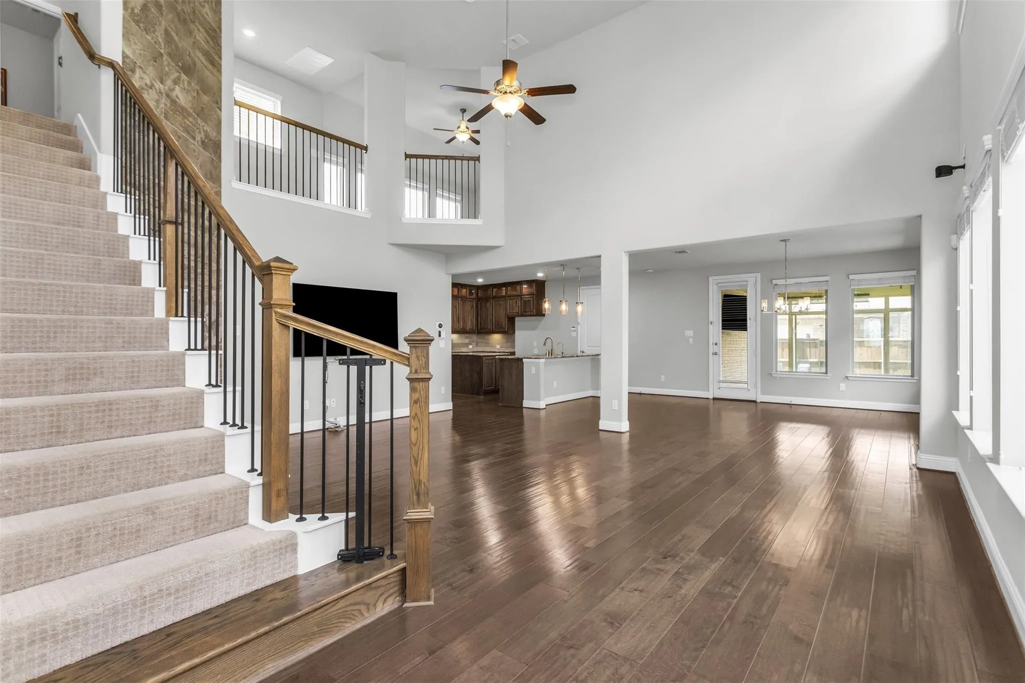 Two-story ceilings, wood-finish flooring, staircase with wood handrails and wrought iron balusters, recessed lighting, and ceiling fans