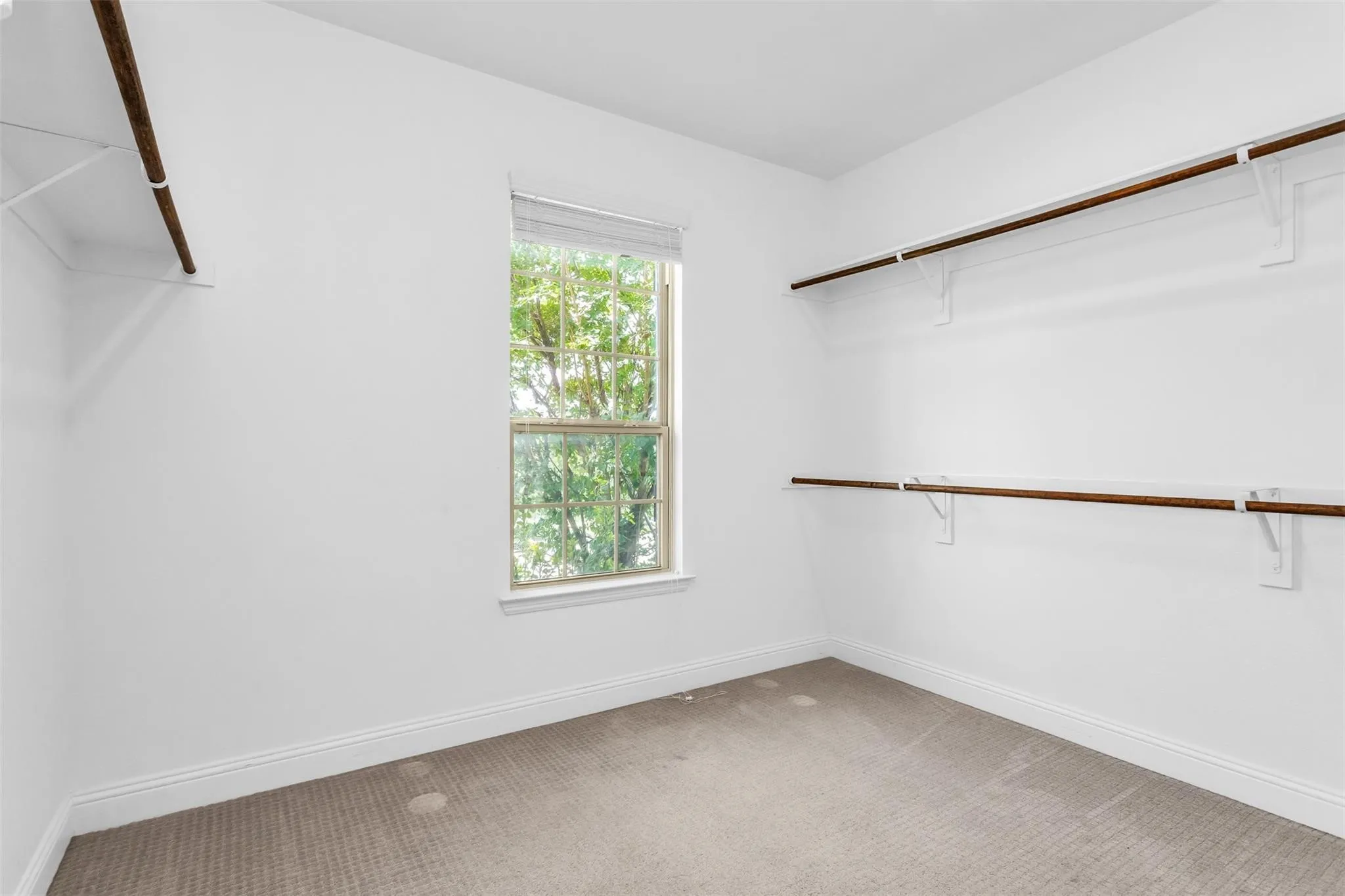 Recessed window with white trim, wall-mounted shelving, and wood finish hanging rods
