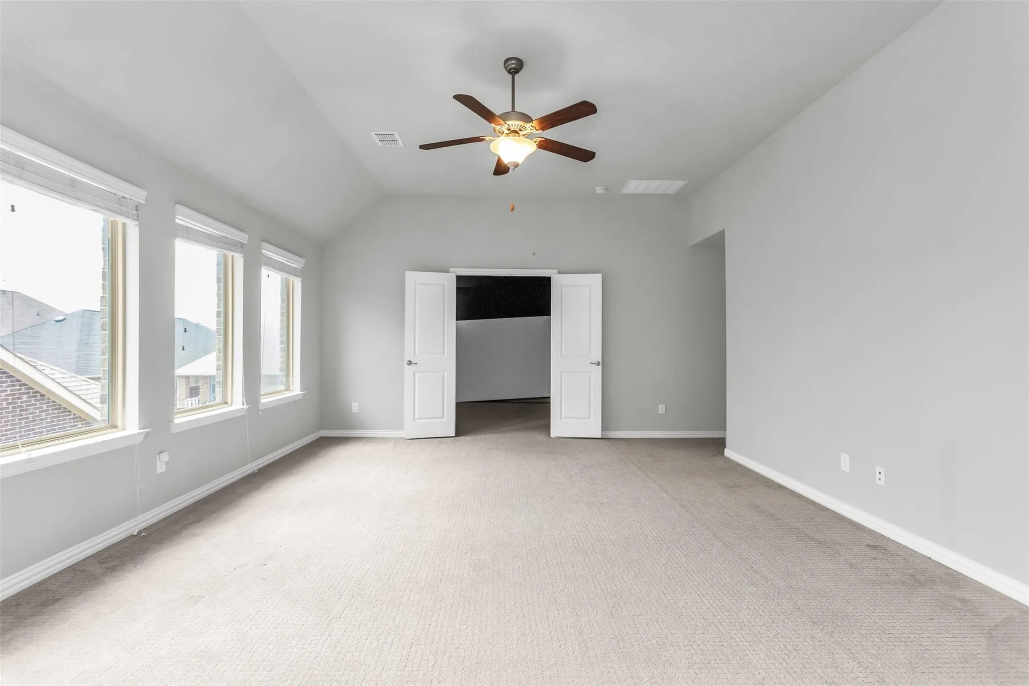 Spacious room featuring vaulted ceilings, a ceiling fan, three large windows, light-colored carpet, and double doors