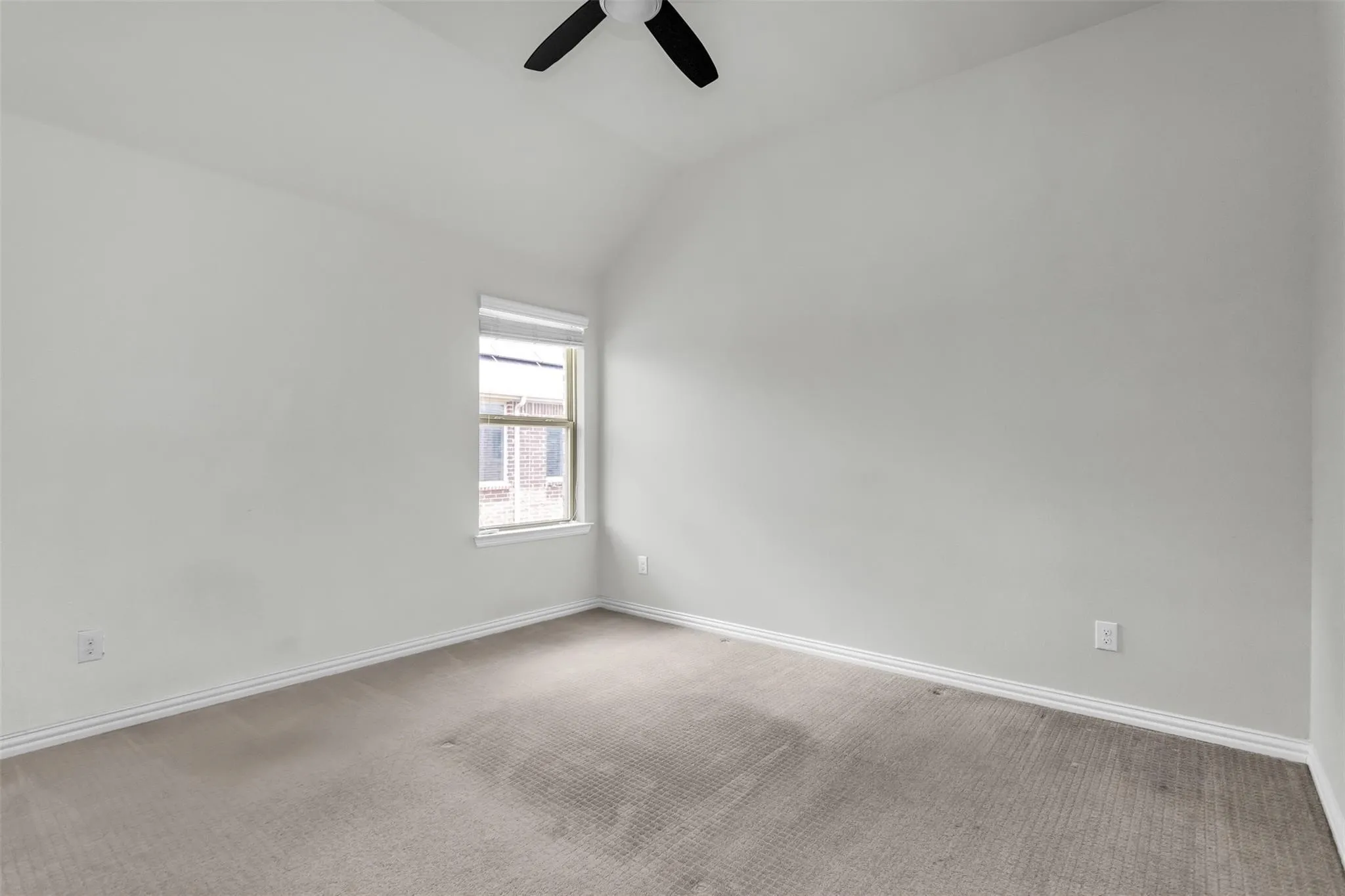 Vaulted ceiling, window with white blinds, wall-mounted ceiling fan, light gray carpeting, and white baseboards