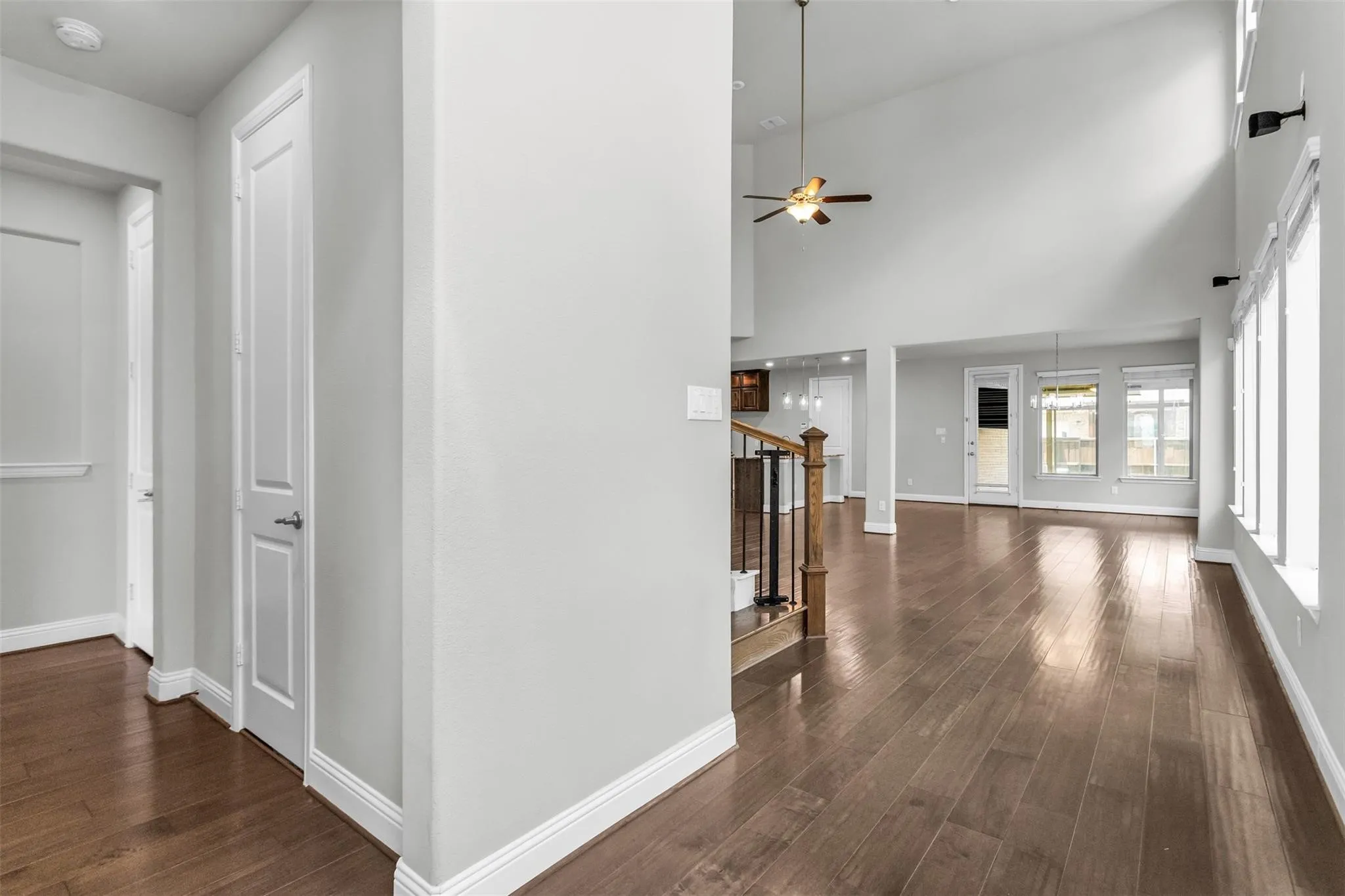 Expansive living area featuring soaring ceilings, wood-finish flooring, multiple windows, a ceiling fan, and a staircase with wood and metal railing
