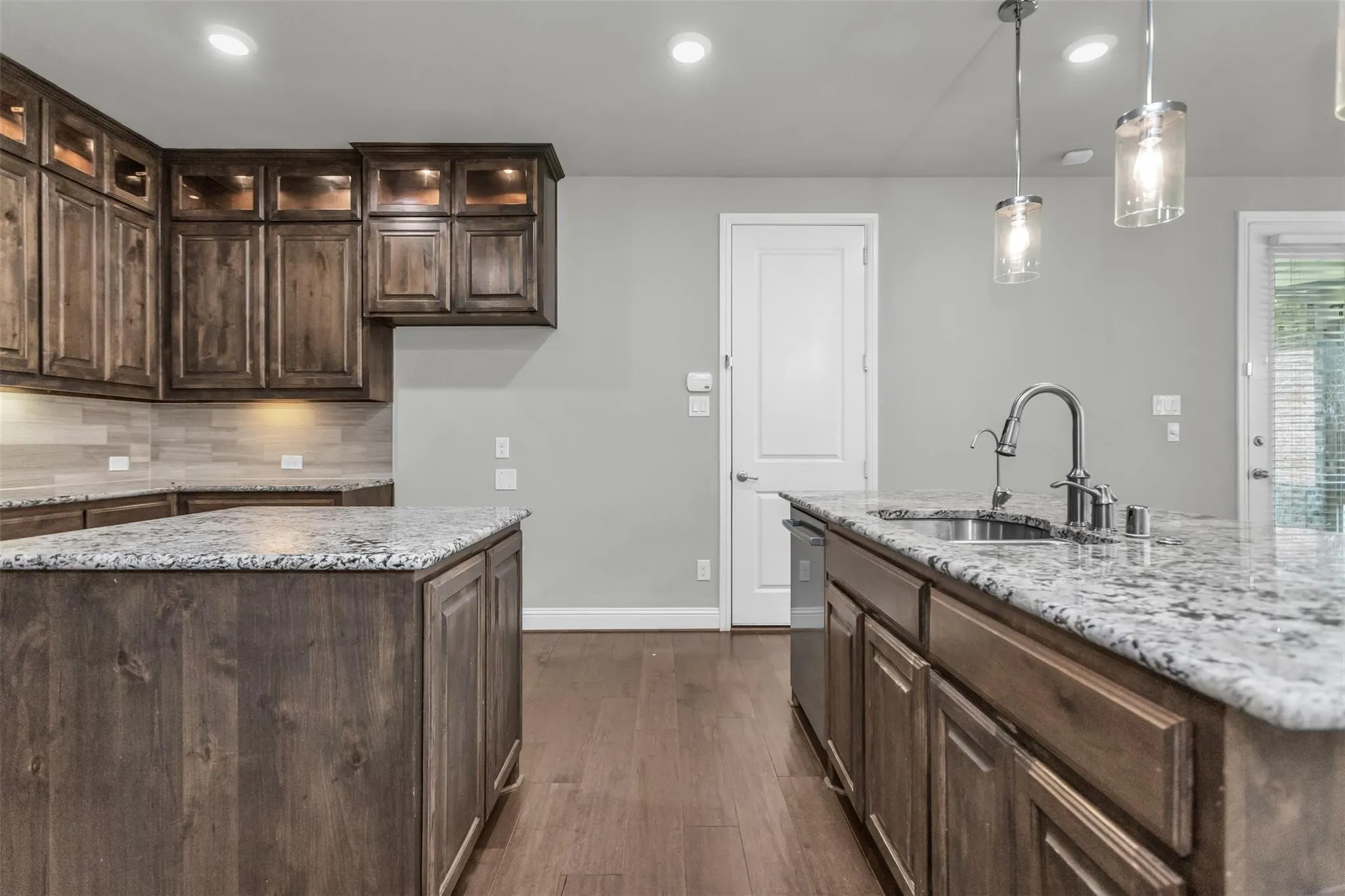 Kitchen featuring two islands with stone countertops, wood-finish flooring, and pendant lighting