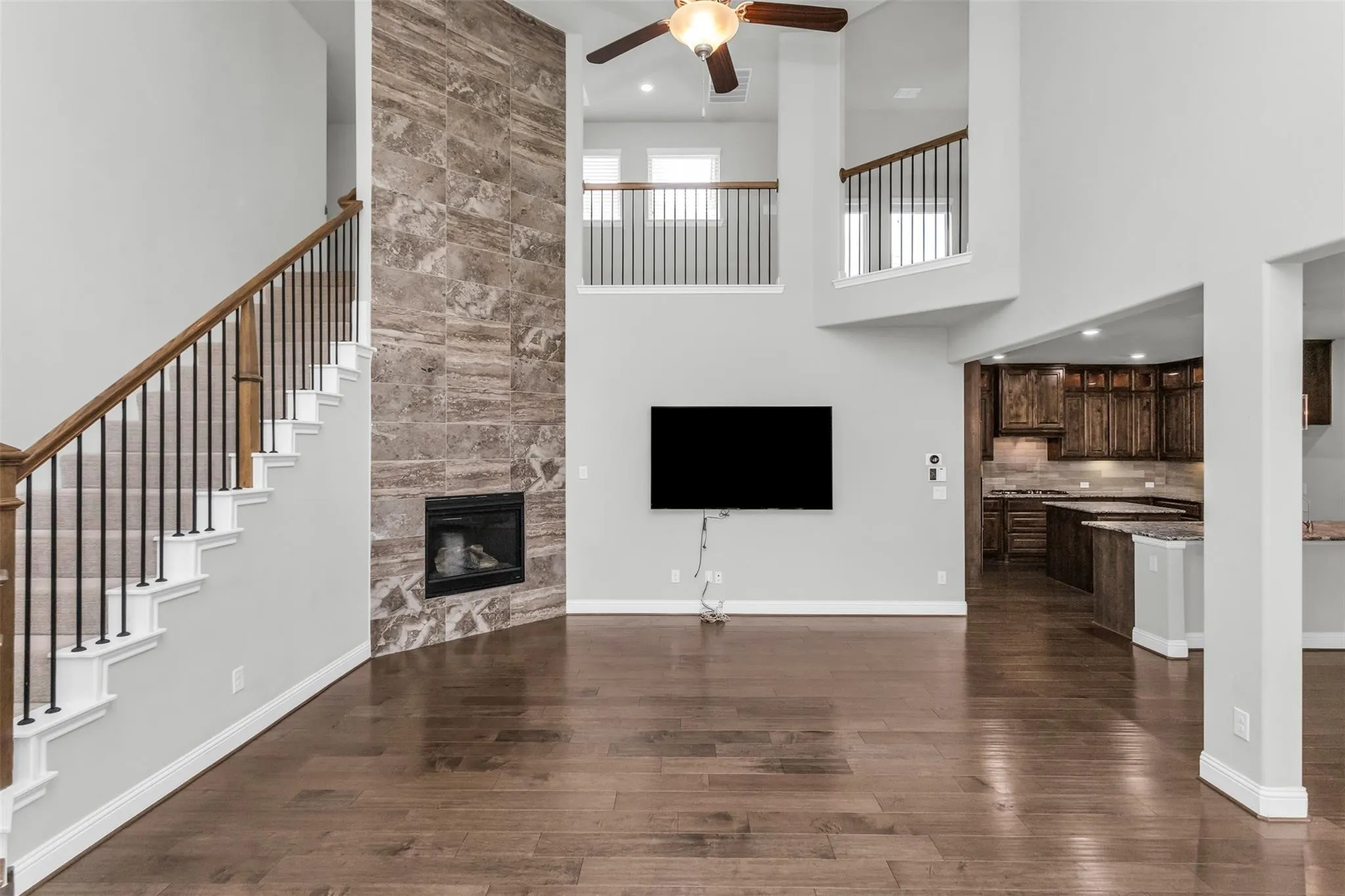 Two-story living area with high ceilings, wood-finish flooring, a stone-clad fireplace, and an open balcony overlooking the space