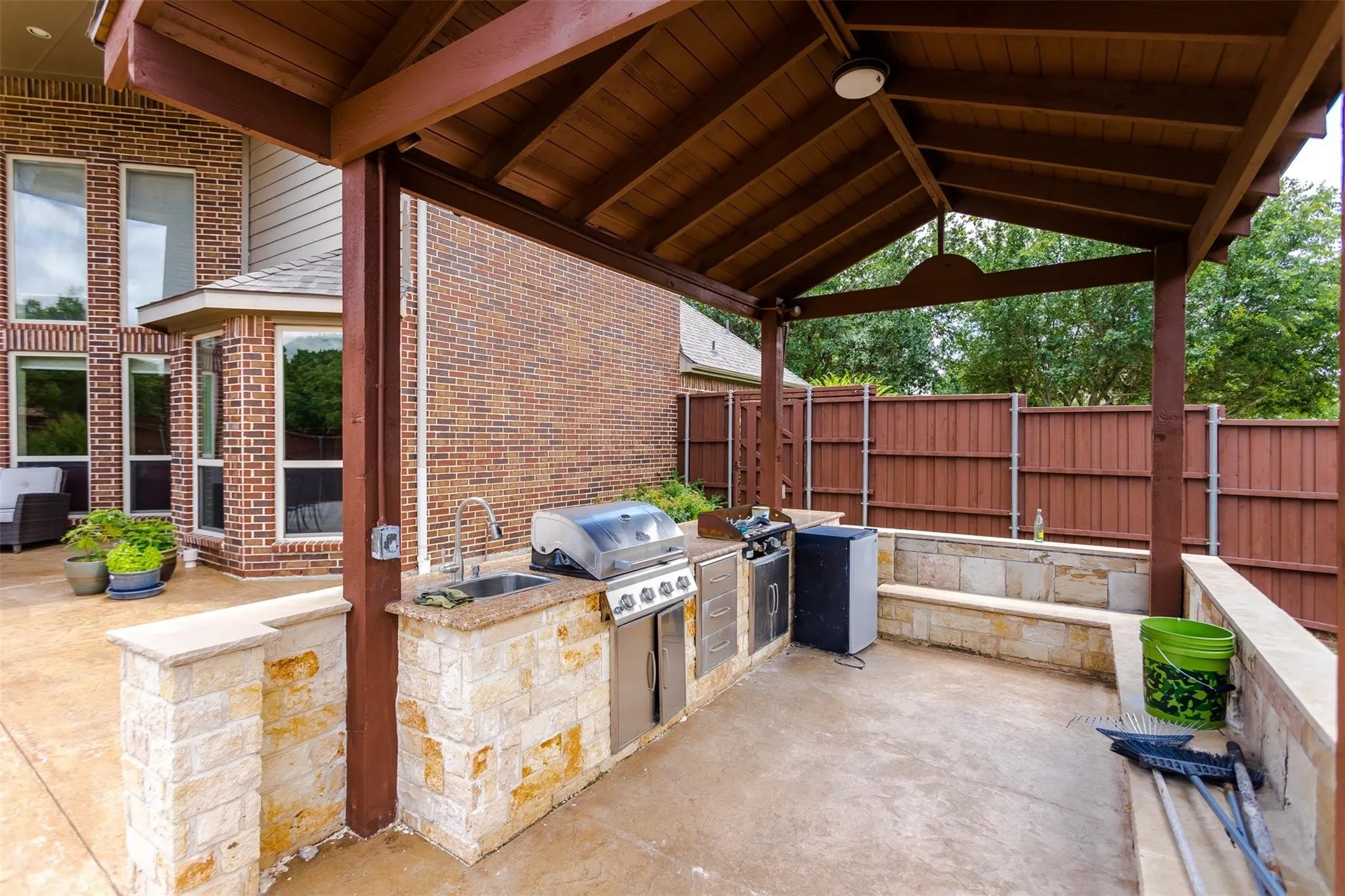 Covered outdoor kitchen featuring stone masonry, built-in grill, sink, and wood-slat ceiling