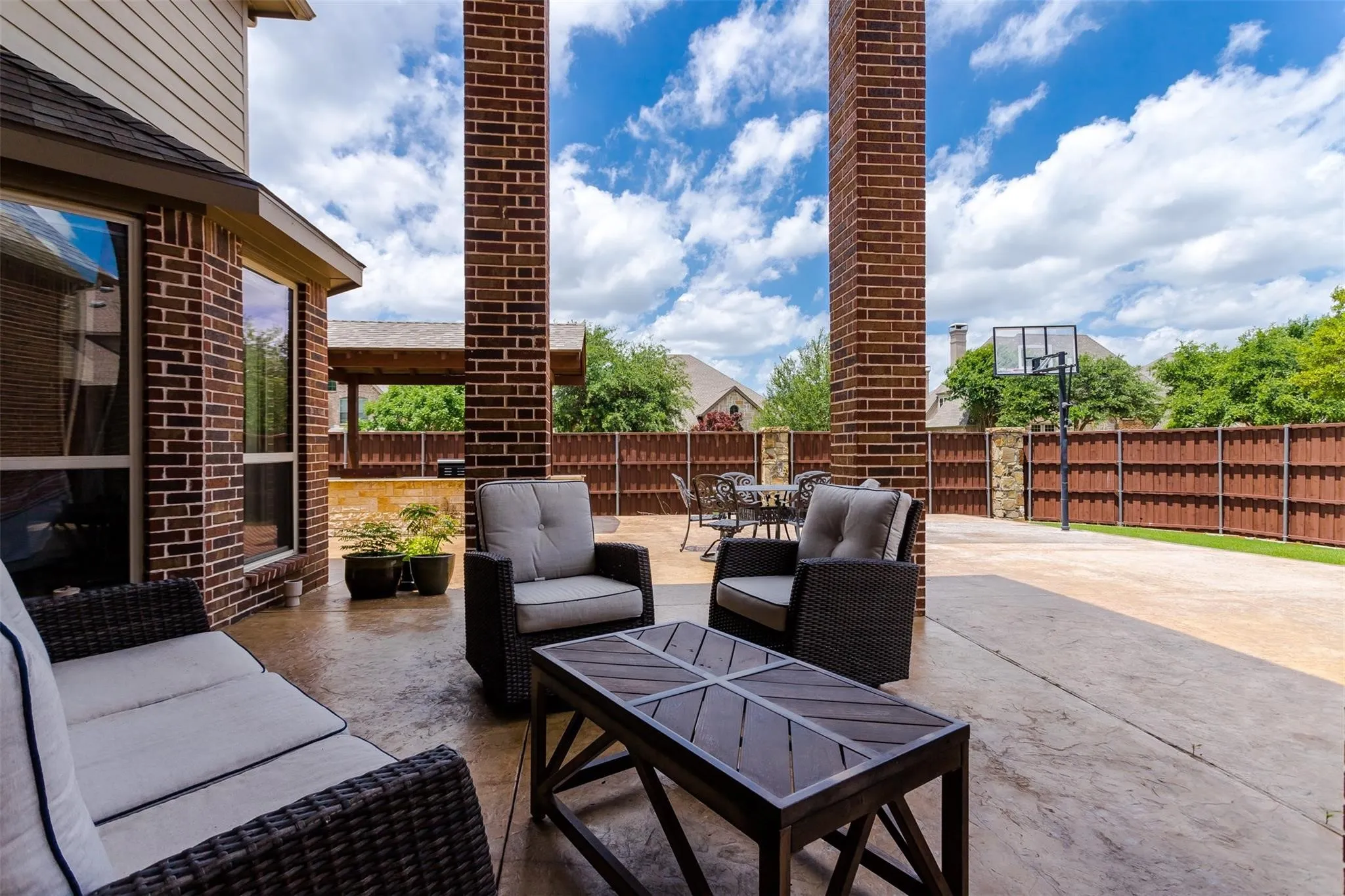 Expansive backyard patio featuring brick architectural pillars, a large concrete pad, privacy fencing, and a built-in outdoor cooking area