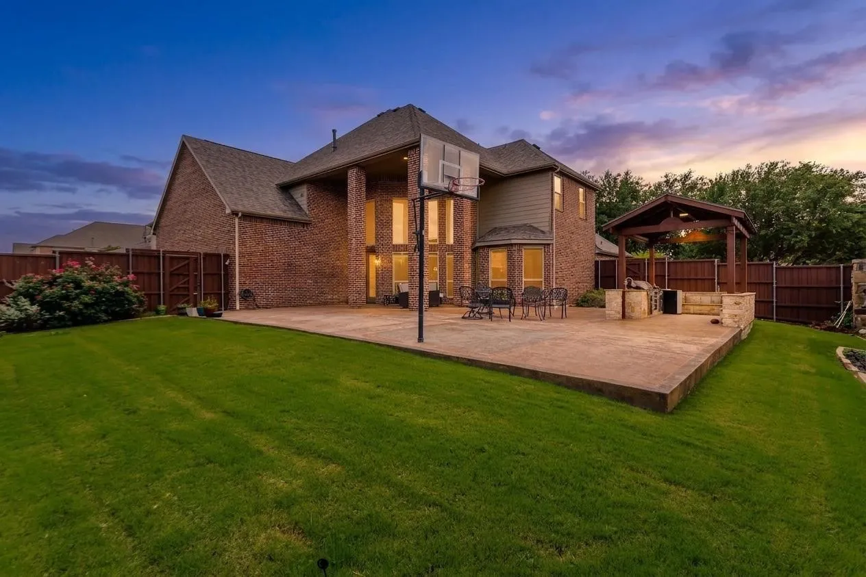 Expansive backyard featuring a large concrete patio, a covered outdoor kitchen structure, and a manicured lawn