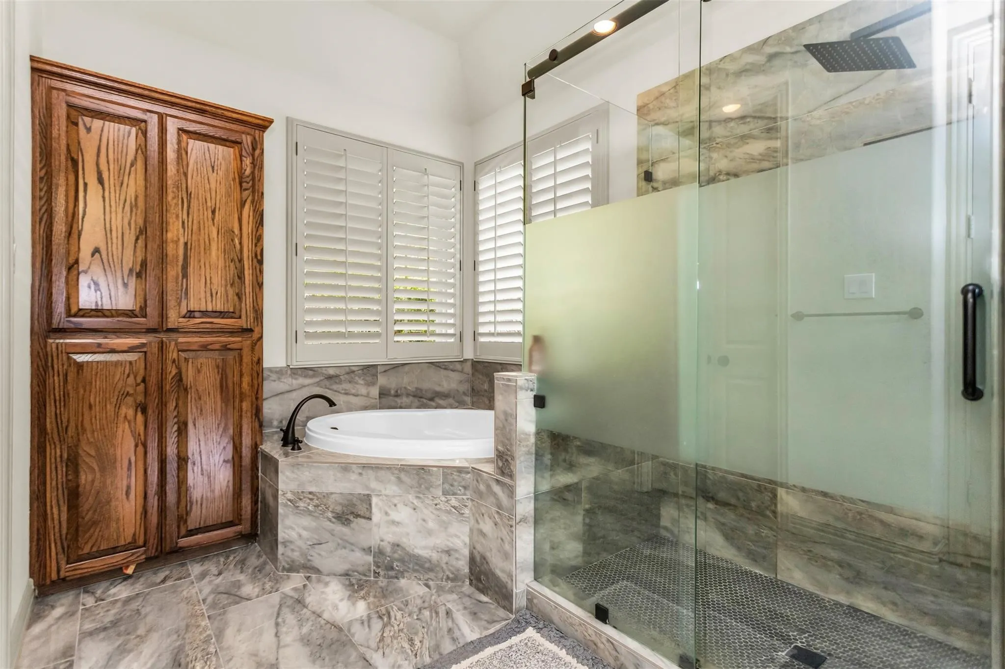Glass-enclosed shower with a matte black rainfall showerhead, and a built-in corner tub with dark bronze fixtures