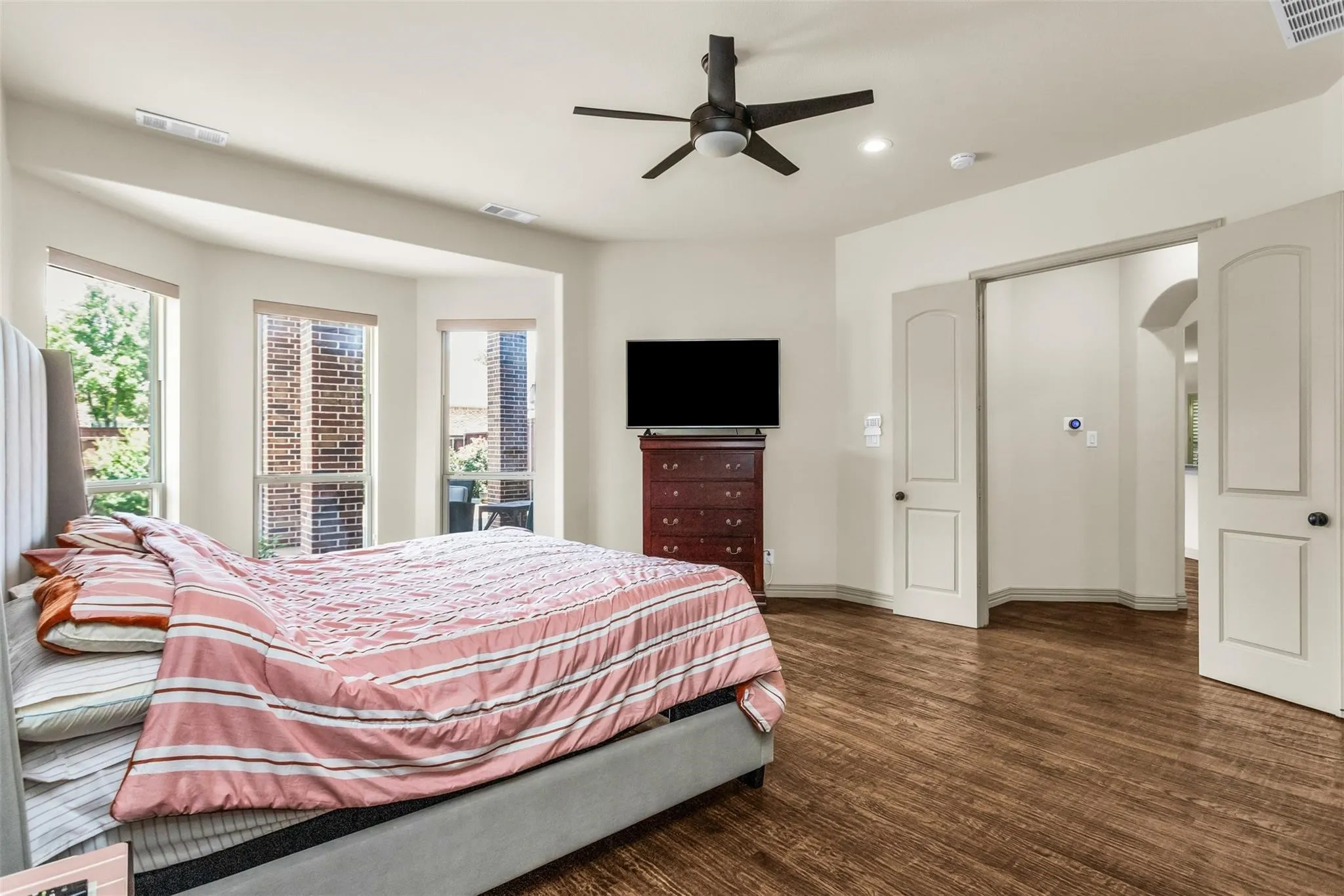 Warm-toned wood-finish flooring, a modern ceiling fan, recessed lighting, double panel doors, and a bay window