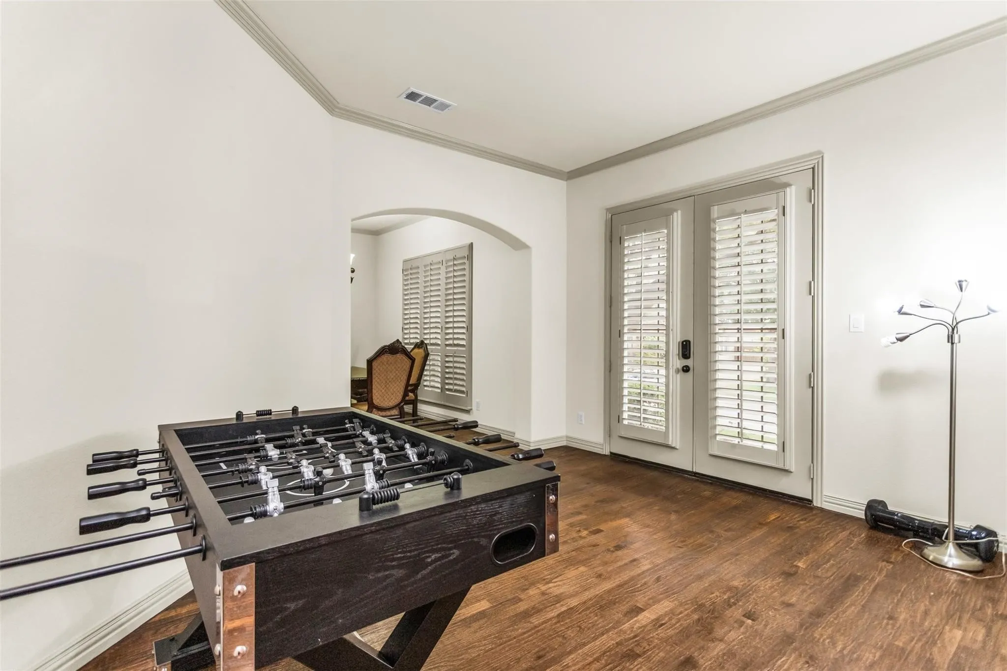 Wood-finish flooring, white walls, crown molding, double French doors, and an arched doorway