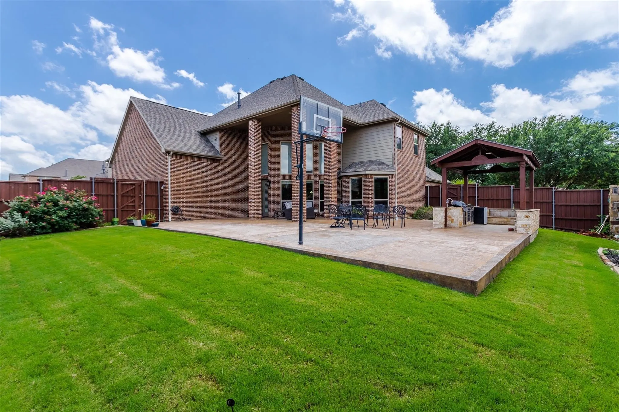 Expansive backyard featuring a manicured lawn, a large concrete patio, and a covered outdoor kitchen area with built-in stone elements