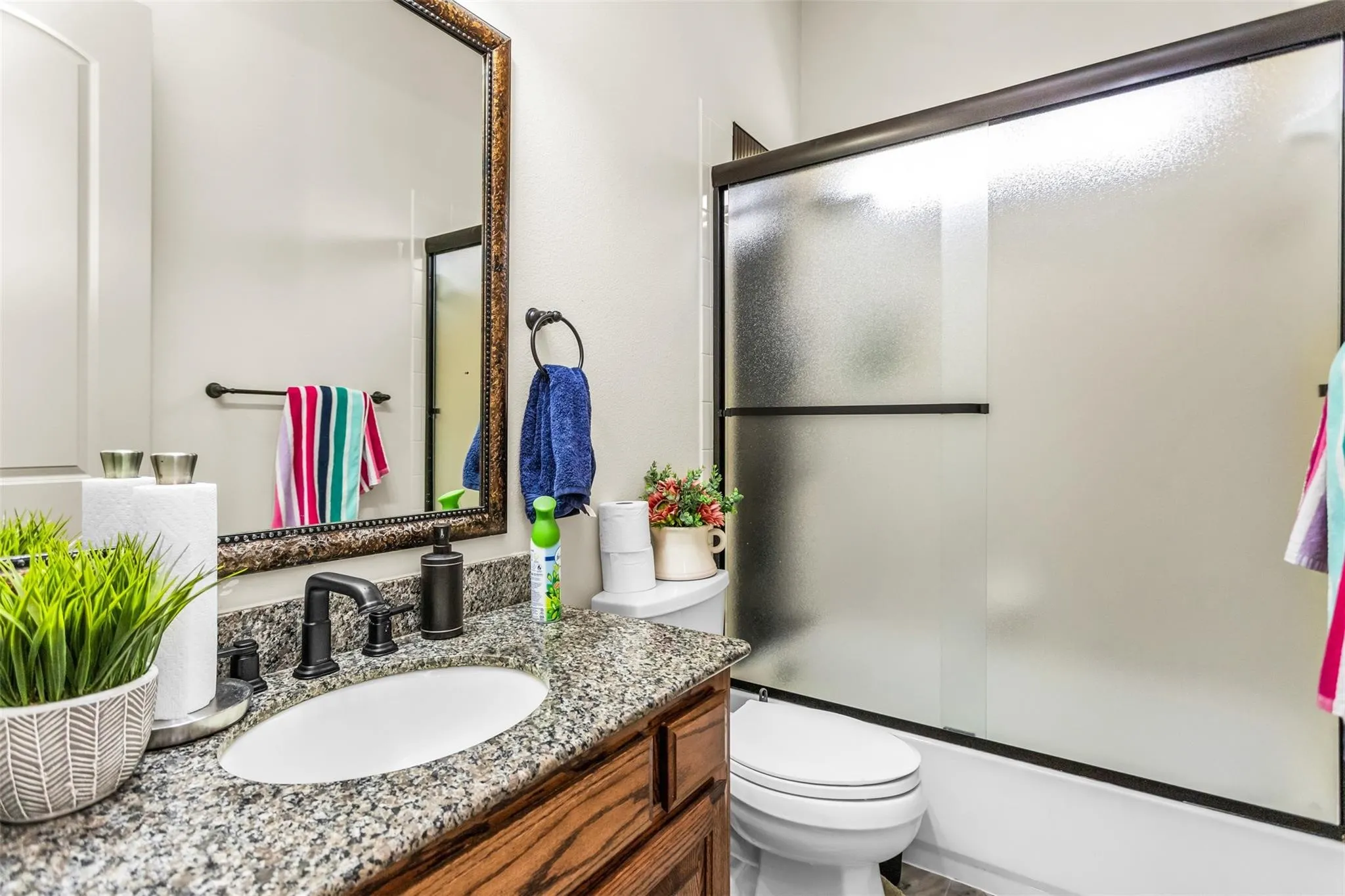 Granite-finish countertop with an oval undermount sink, dark-finish faucet, framed mirror, and a shower with a frosted glass door