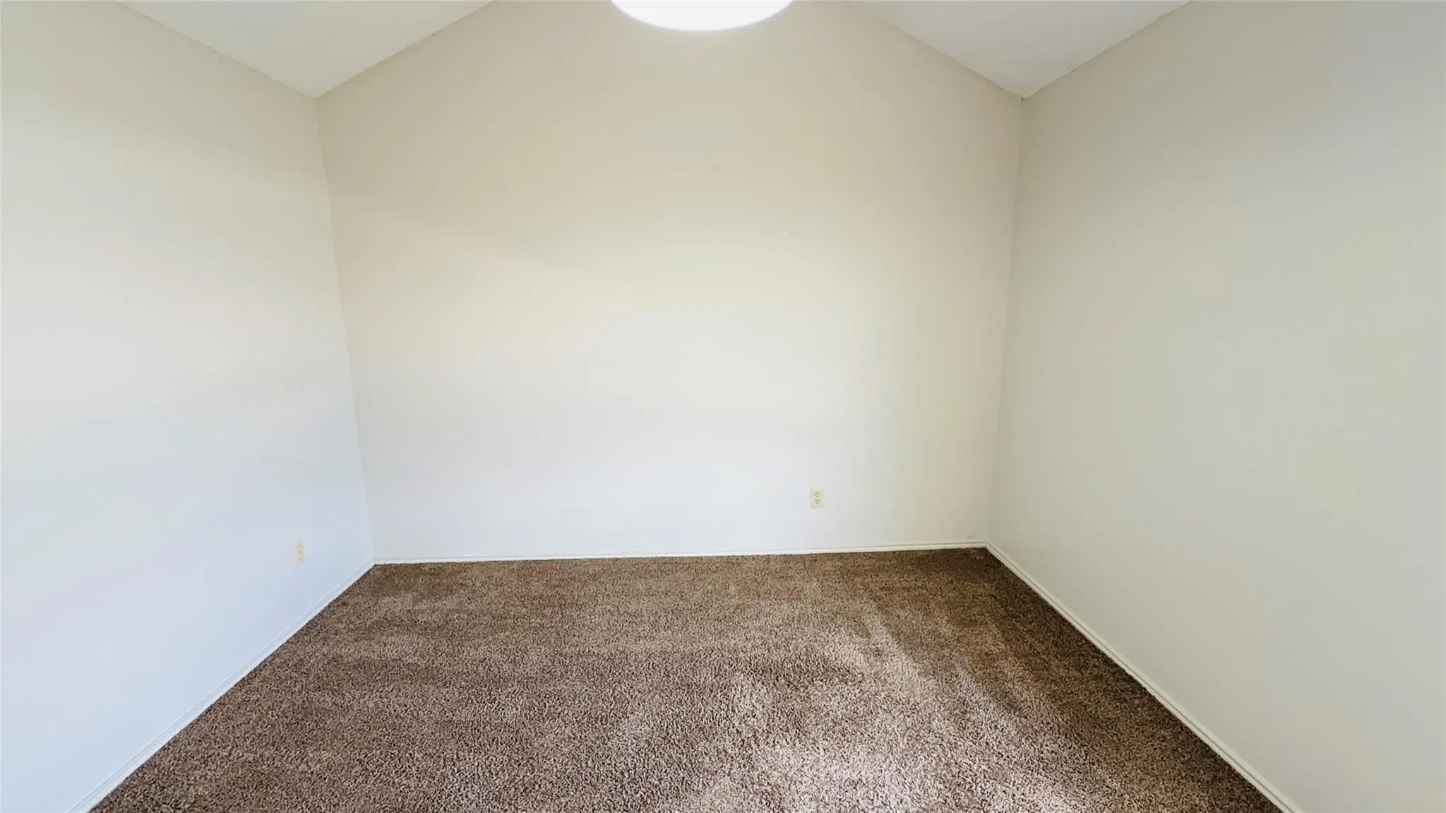 Vaulted ceiling with an attached light fixture, light-colored walls, and neutral carpet flooring