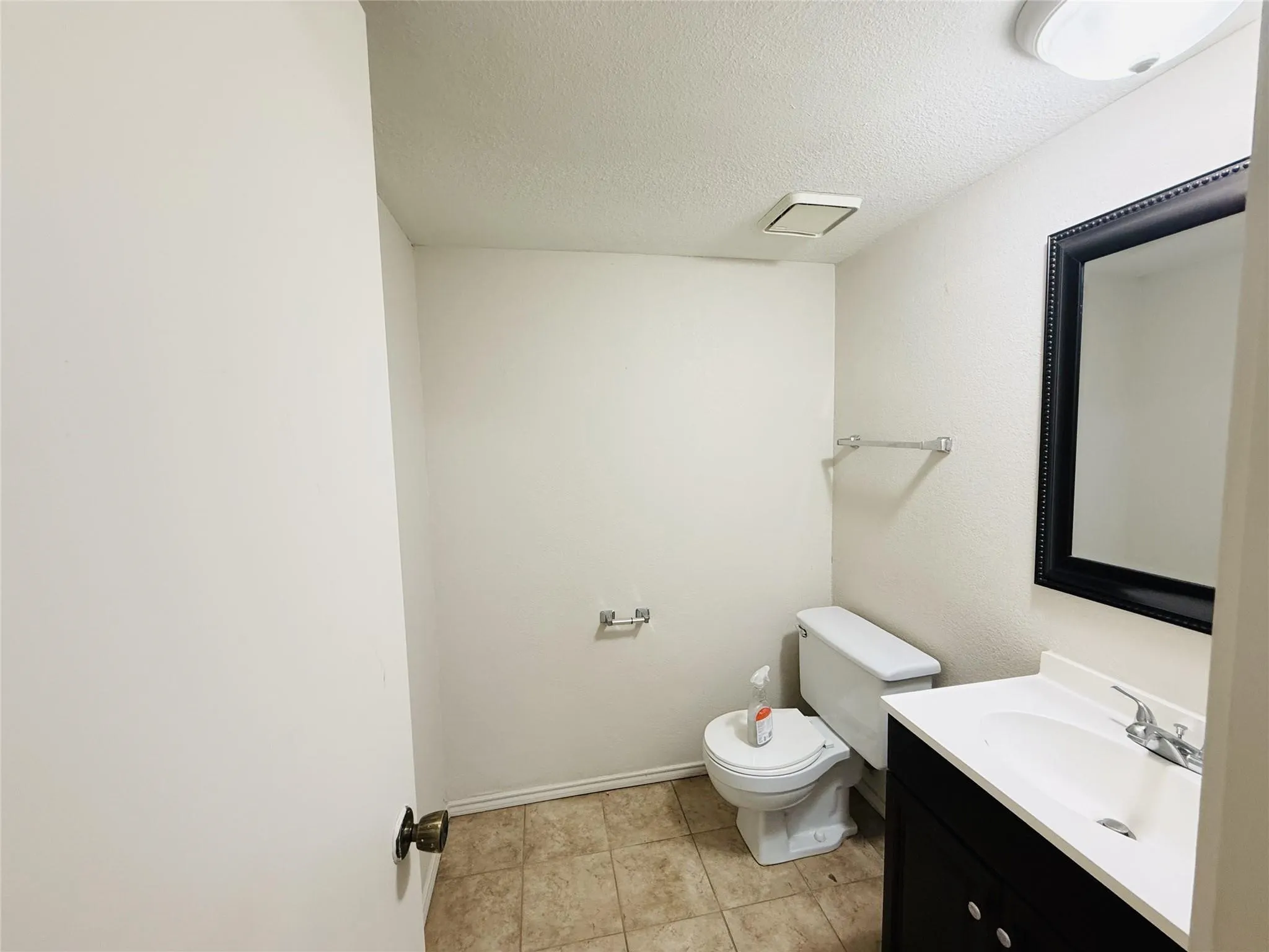 Bathroom featuring a dark wood vanity with white countertop, an integrated sink, a framed mirror, and tiled flooring