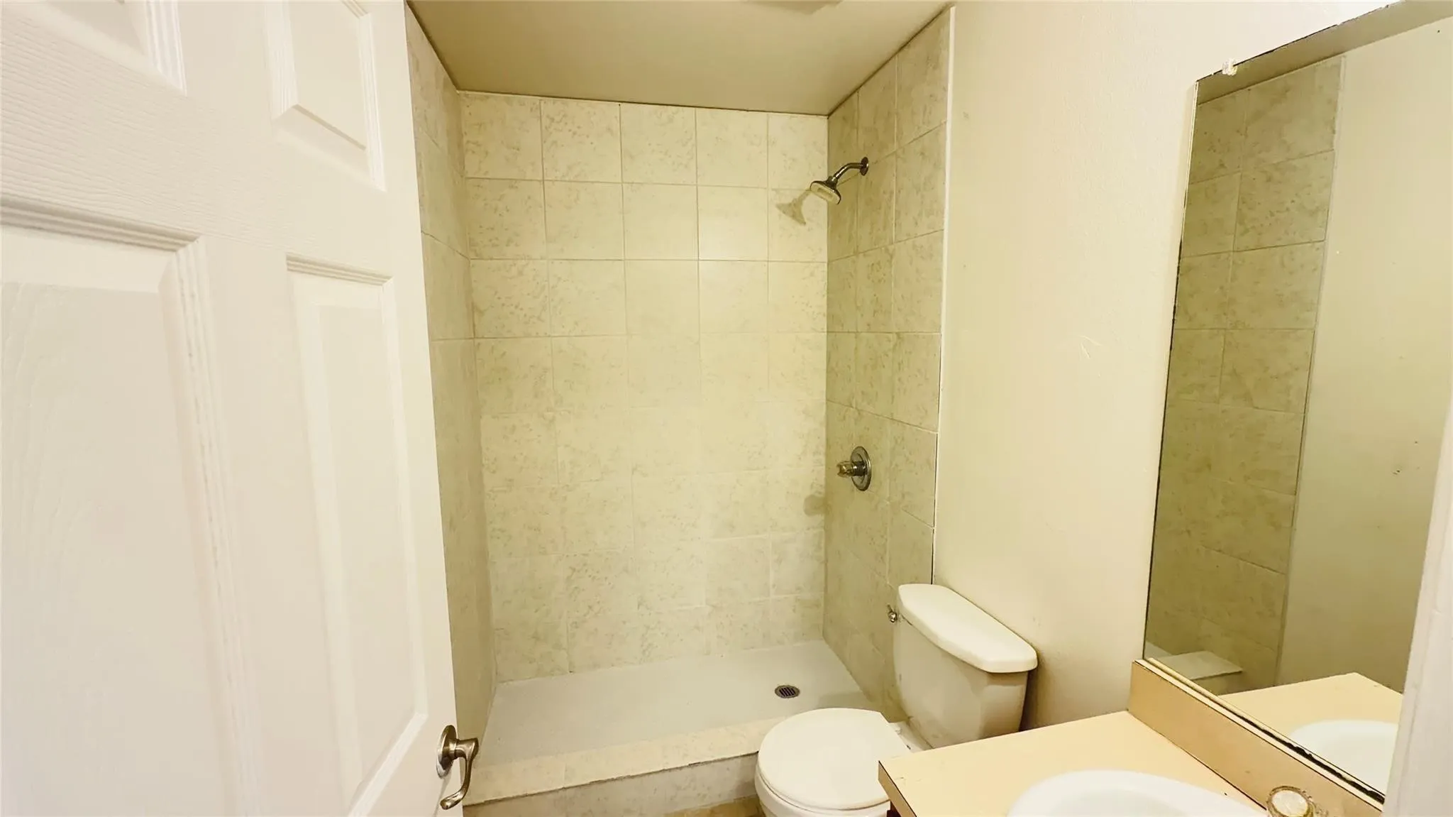 Tiled shower stall with a white shower pan, a wall-mounted shower head, and a toilet with a white tank and bowl