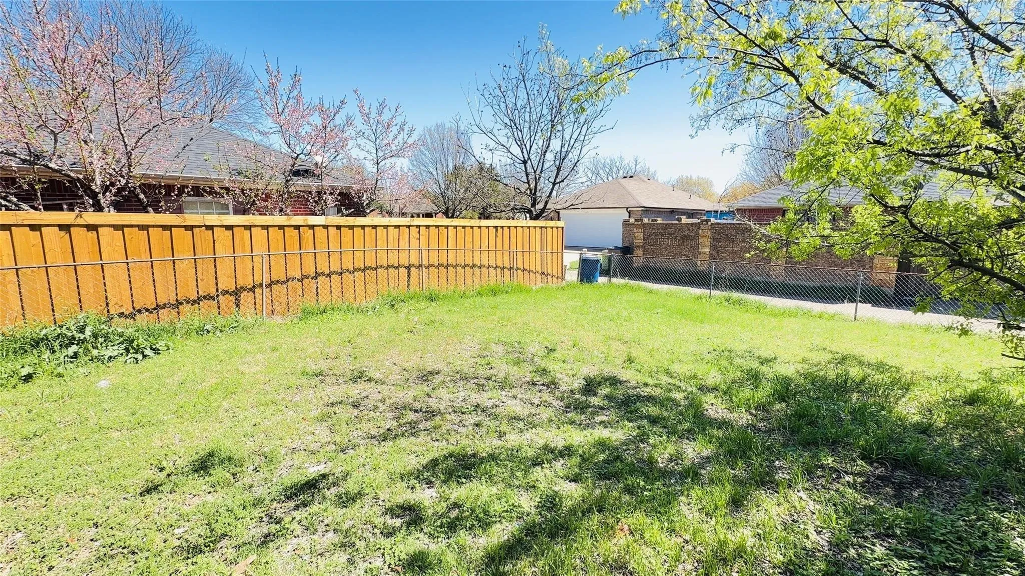 Expansive grassy area with a wood privacy fence and mature trees